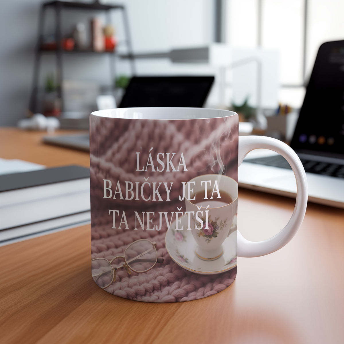 Hrnek s nápisem LÁSKA BABIČKY JE TA NEJVĚTŠÍ na růžovém pleteném pozadí.