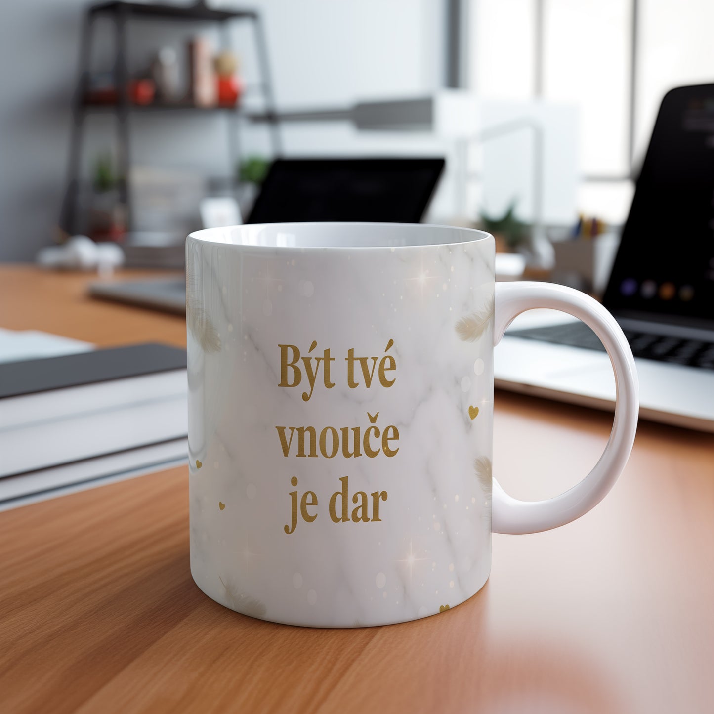 Hrnek s nápisem 'Být tvé vnouče je dar' se zlatými peříčky na mramorovém pozadí.