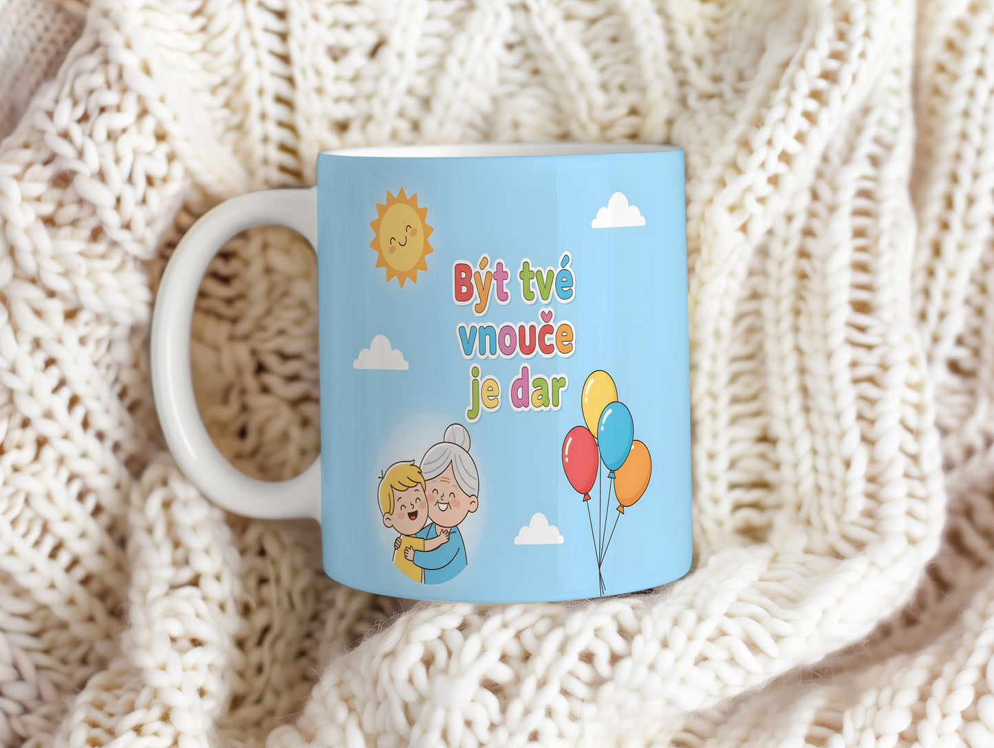 Hrnek s nápisem Být tvé vnouče je dar, sluncem a balónky na modrém pozadí.