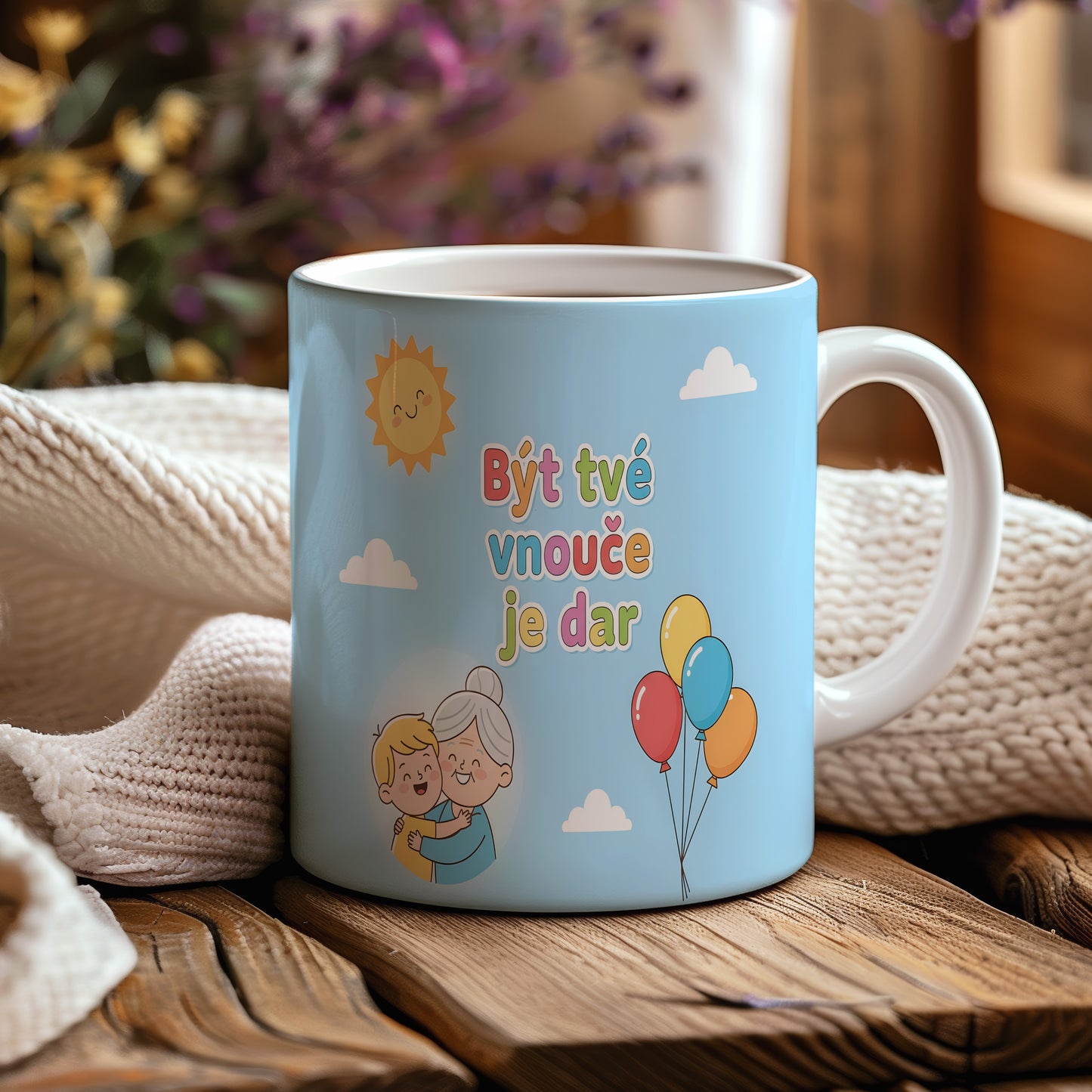 Hrnek s nápisem Být tvé vnouče je dar, sluncem a balónky na modrém pozadí.