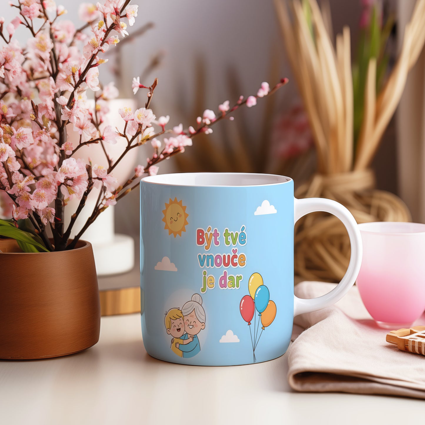Hrnek s nápisem Být tvé vnouče je dar, sluncem a balónky na modrém pozadí.