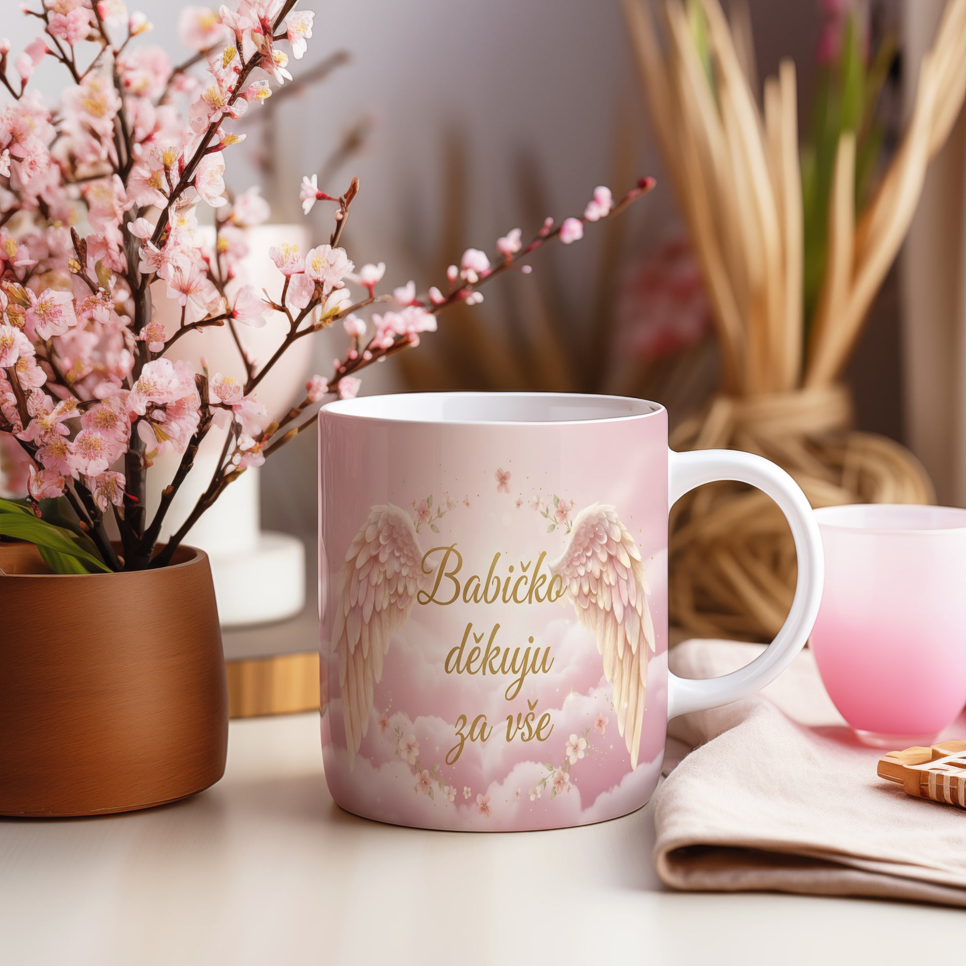 Růžový hrnek s andělskými křídly a květinami.