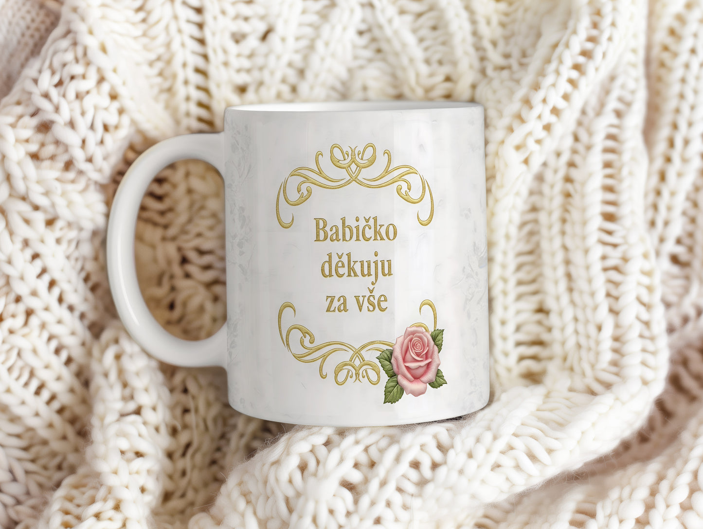 Hrnek s růžovými květy a zlatým textem na mramorovém pozadí.