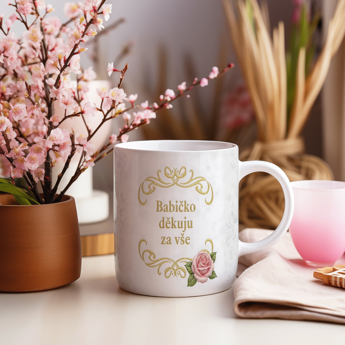 Hrnek s růžovými květy a zlatým textem na mramorovém pozadí.