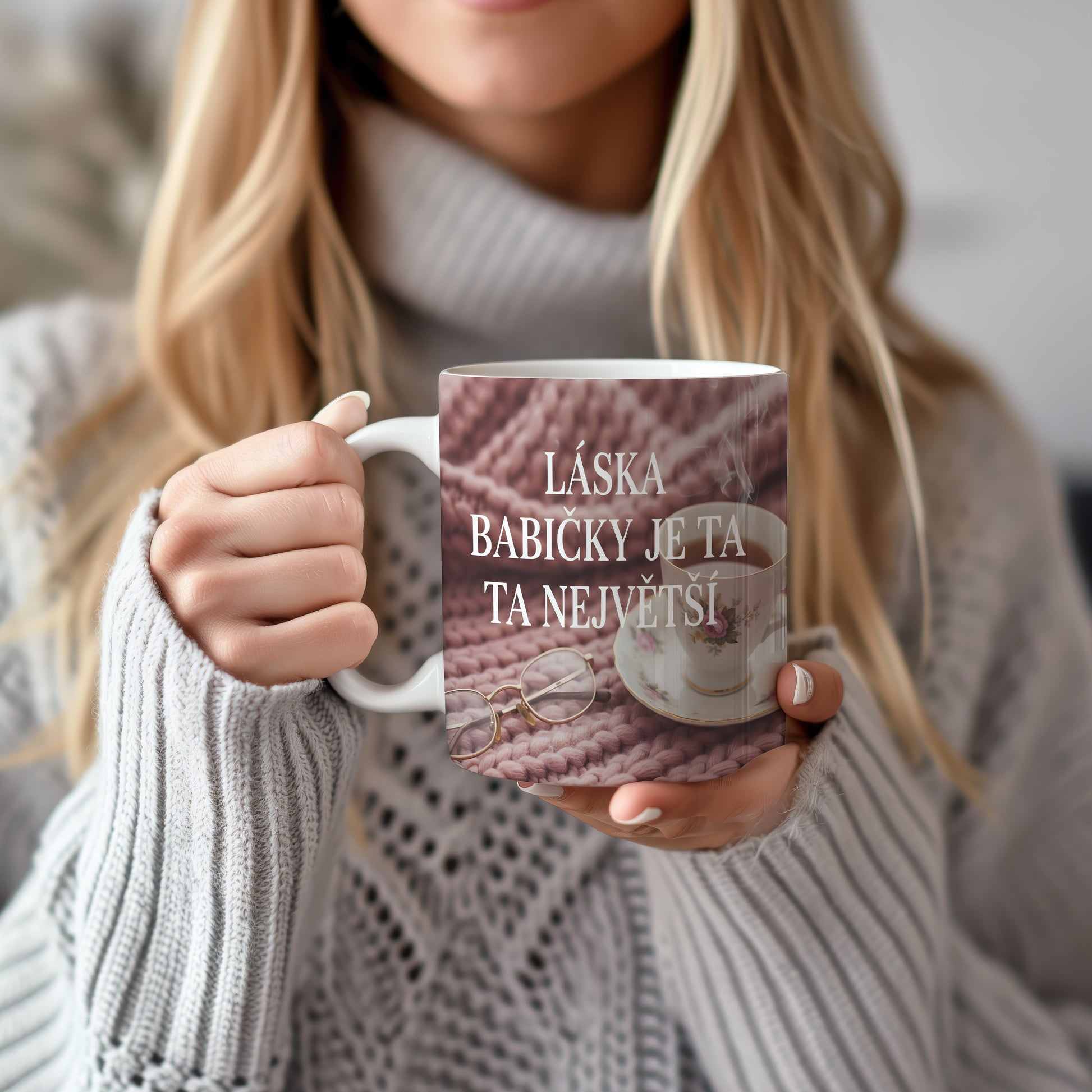 Hrnek s nápisem LÁSKA BABIČKY JE TA NEJVĚTŠÍ na růžovém pleteném pozadí.