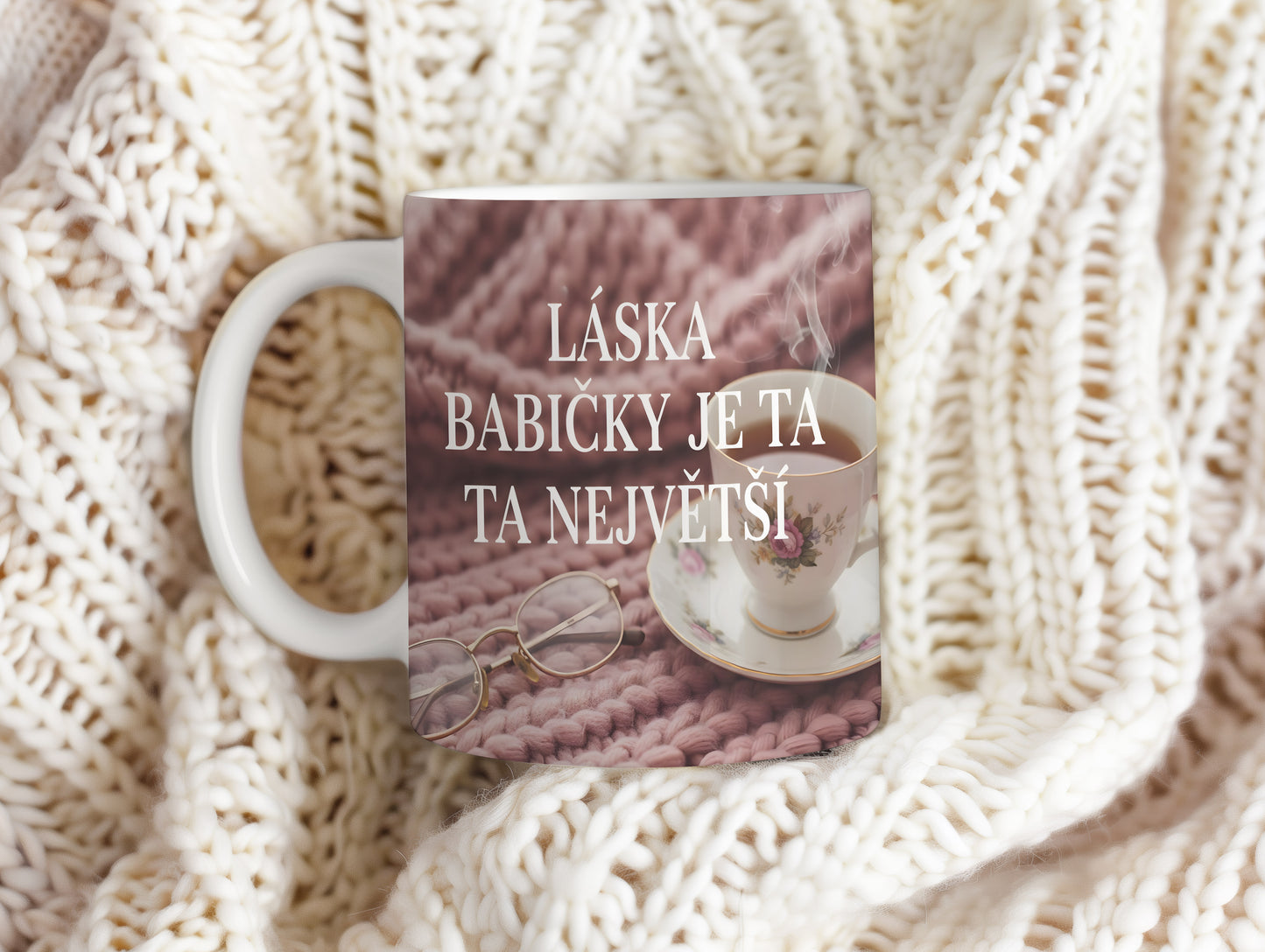 Hrnek s nápisem LÁSKA BABIČKY JE TA NEJVĚTŠÍ na růžovém pleteném pozadí.