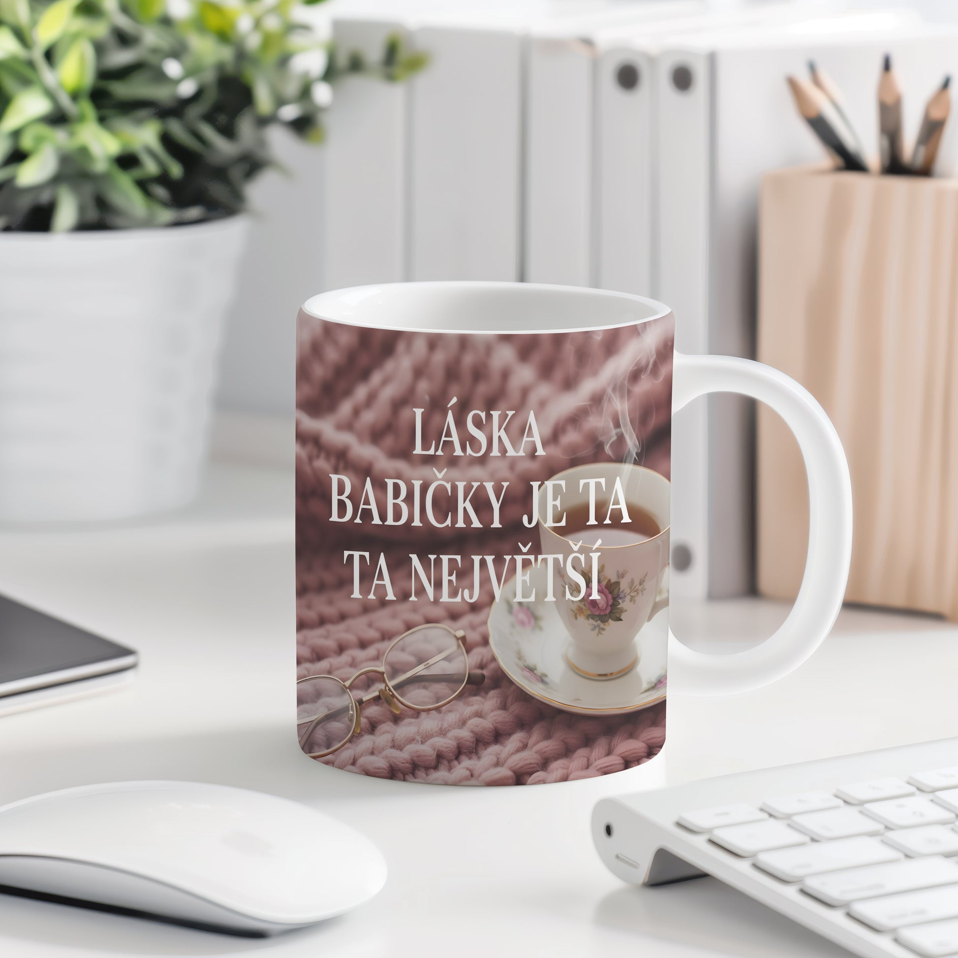 Hrnek s nápisem LÁSKA BABIČKY JE TA NEJVĚTŠÍ na růžovém pleteném pozadí.