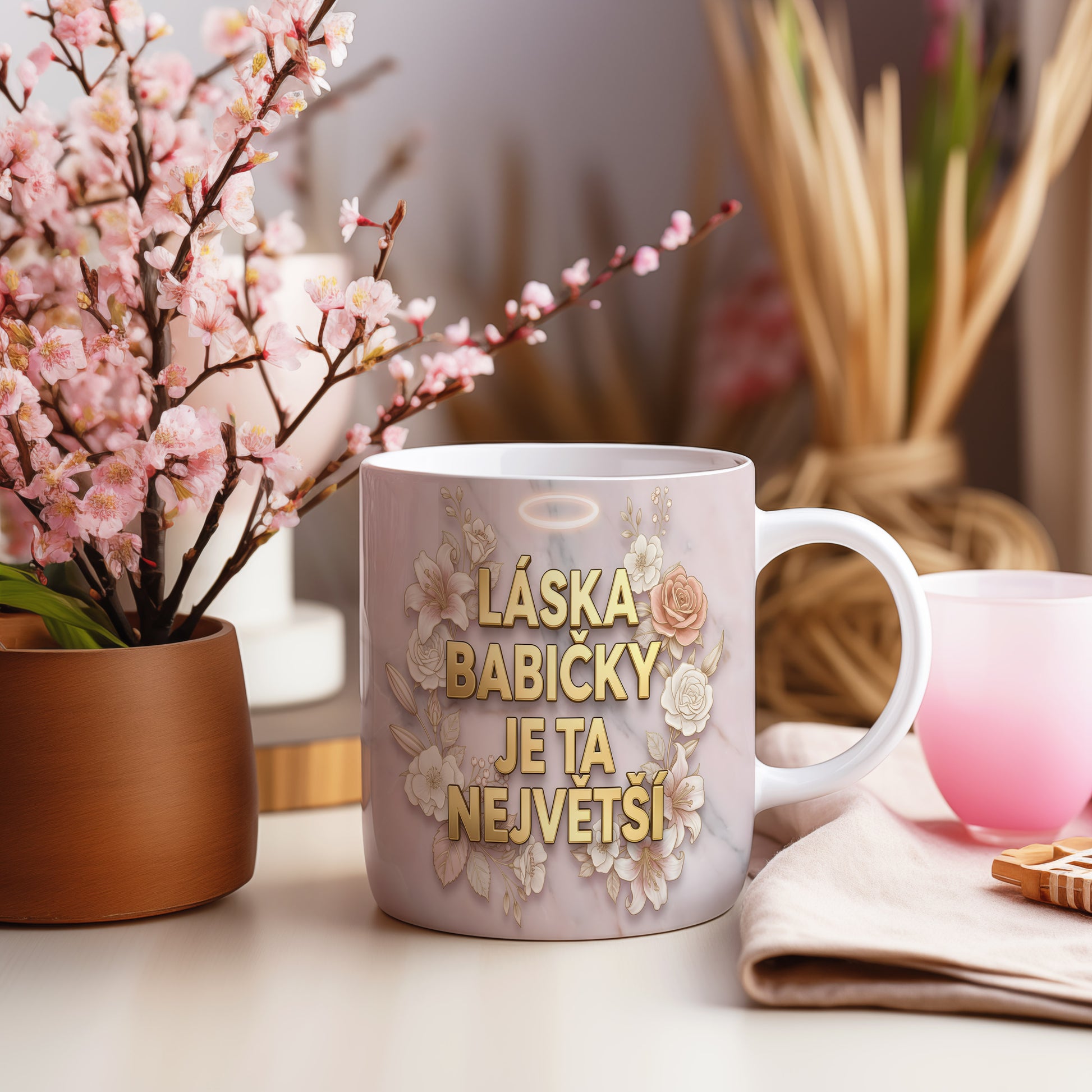 Hrnek s nápisem LÁSKA BABIČKY JE TA NEJVĚTŠÍ na mramorovém pozadí s květinami.