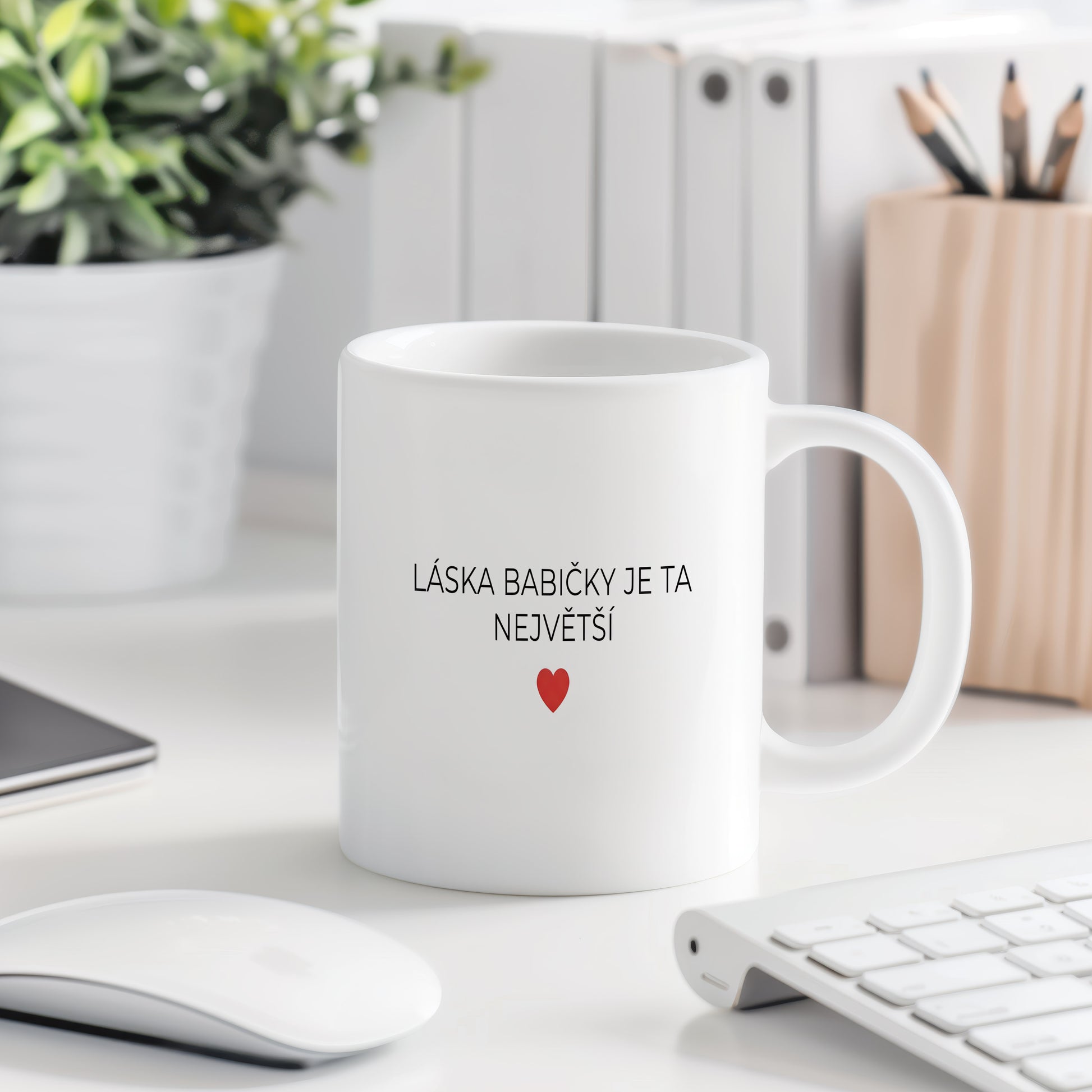 Bílý hrnek s nápisem 'LÁSKA BABIČKY JE TA NEJVĚTŠÍ' a červeným srdcem.