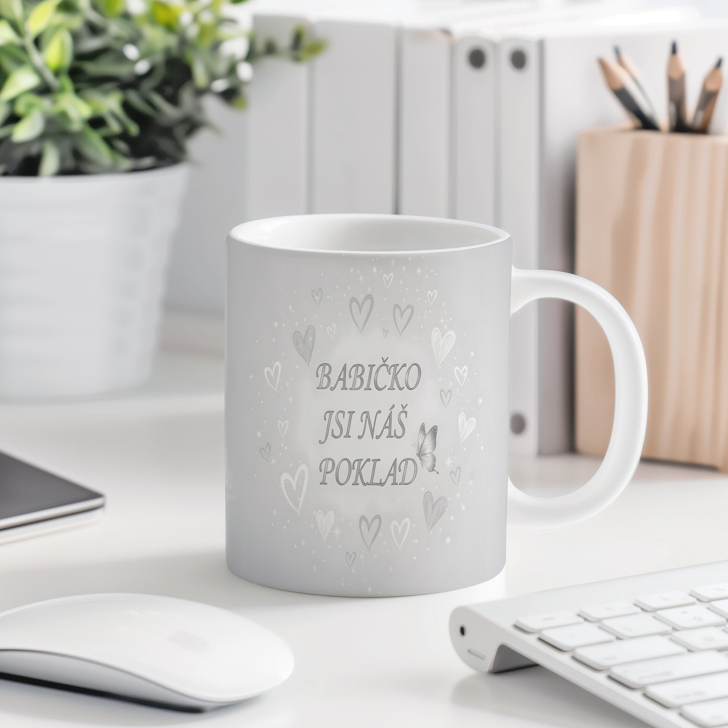 Hrnek s nápisem BABIČKO JSI NÁŠ POKLAD, ozdobený srdci a motýlem.