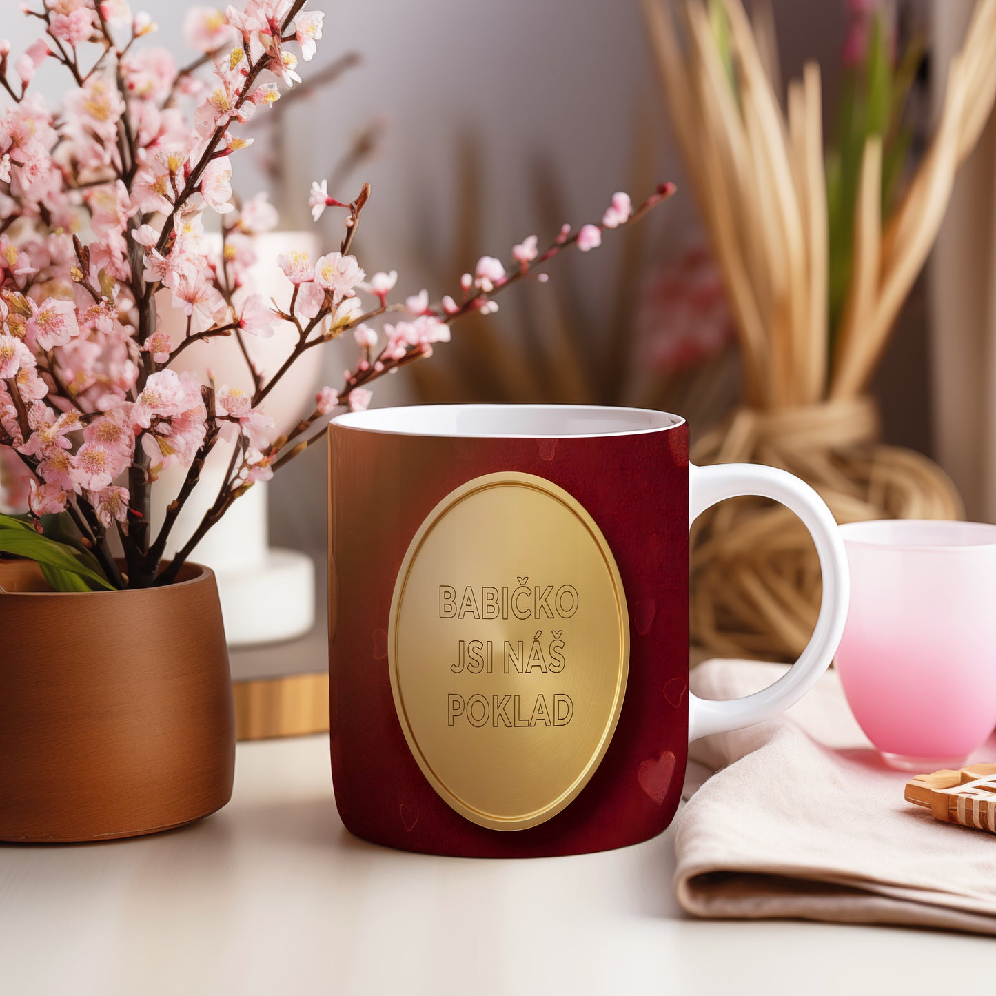 Hrnek s nápisem BABIČKO JSI NÁŠ POKLAD na červeném pozadí se zlatým medailonem.