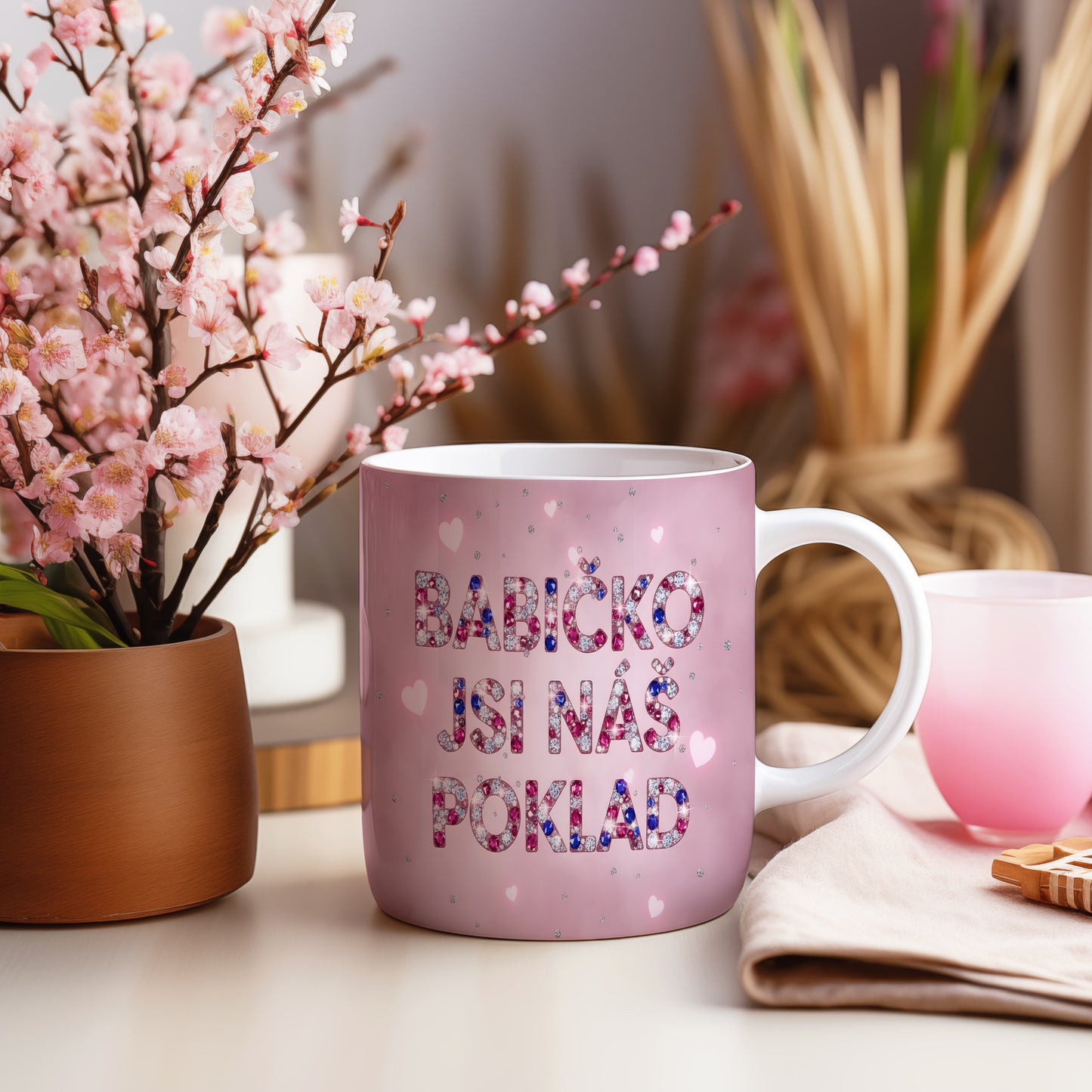 Růžový hrnek s nápisem 'BABIČKO JSI NÁŠ POKLAD' a třpytivými srdíčky.