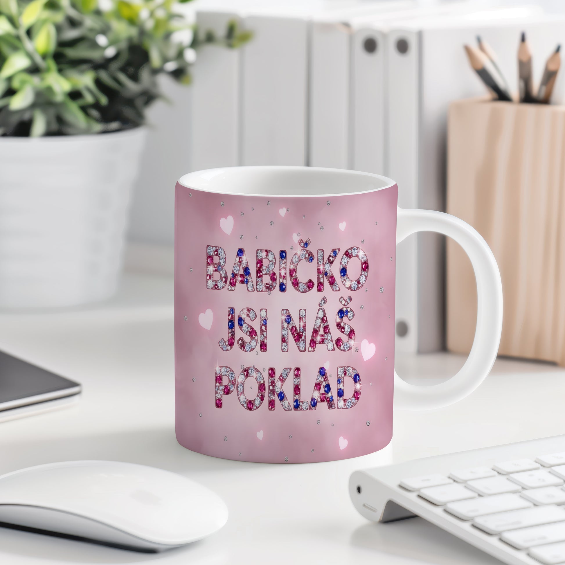 Růžový hrnek s nápisem 'BABIČKO JSI NÁŠ POKLAD' a třpytivými srdíčky.