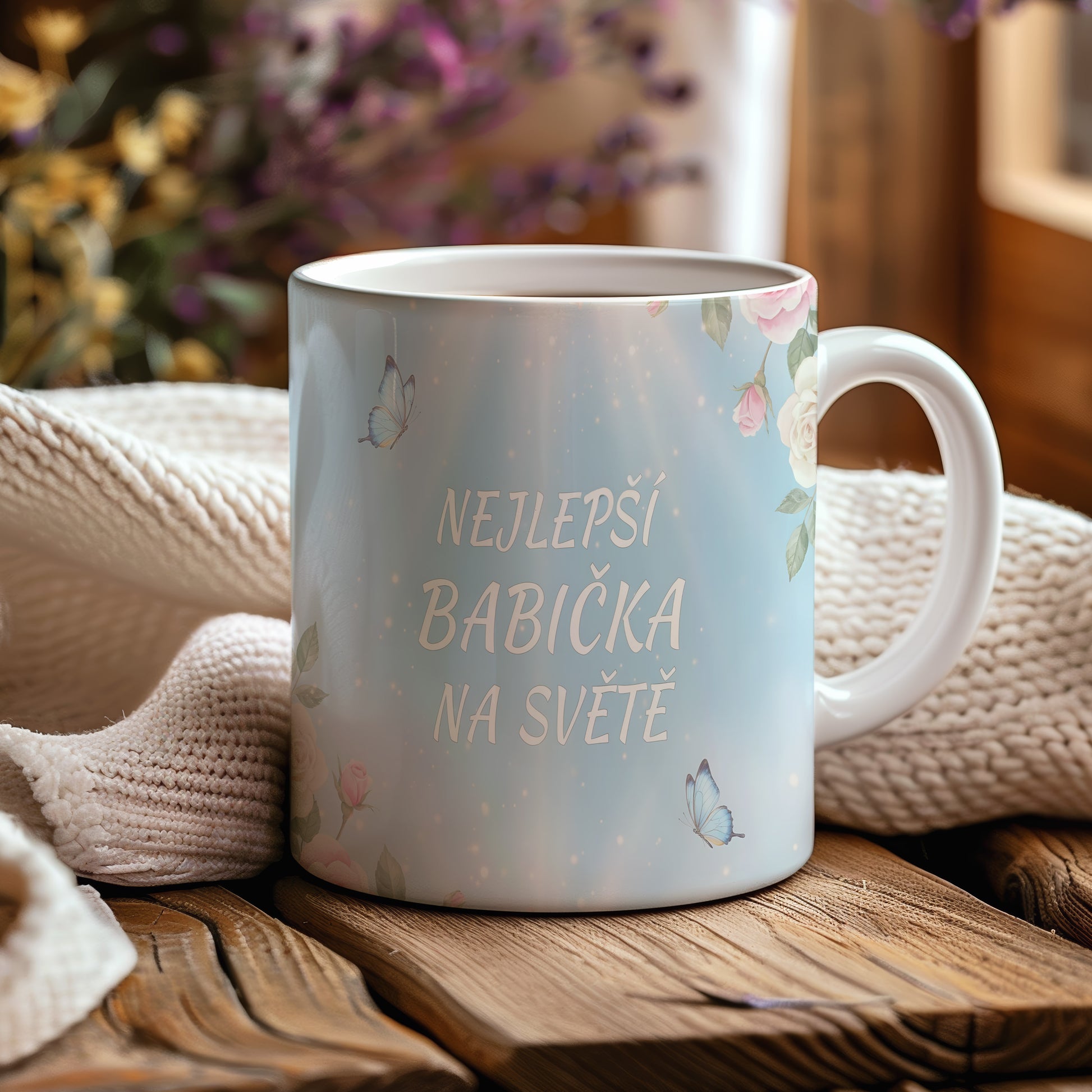 Hrnek s nápisem 'NEJLEPŠÍ BABIČKA NA SVĚTĚ', zdobený motýly a květinami.