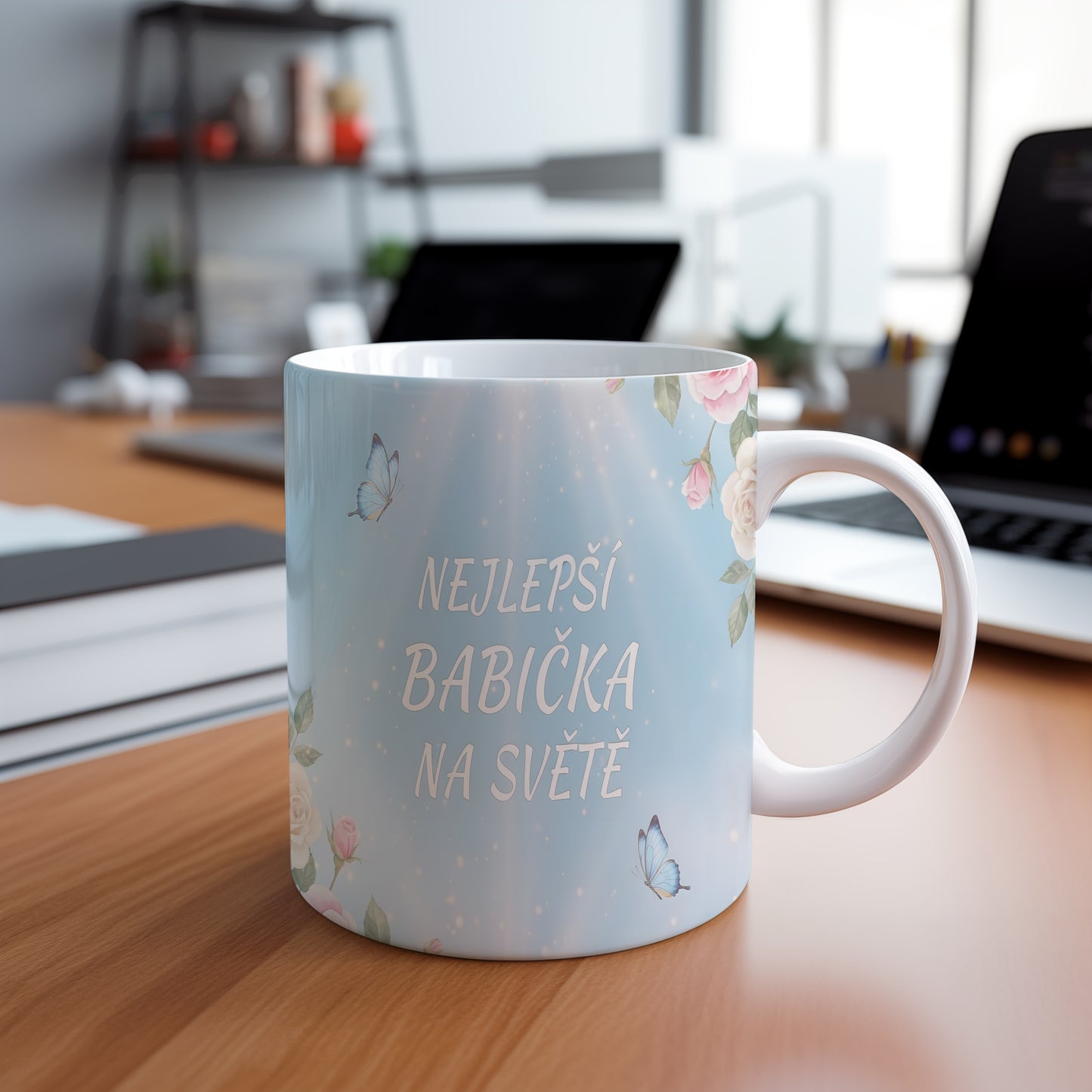 Hrnek s nápisem 'NEJLEPŠÍ BABIČKA NA SVĚTĚ', zdobený motýly a květinami.