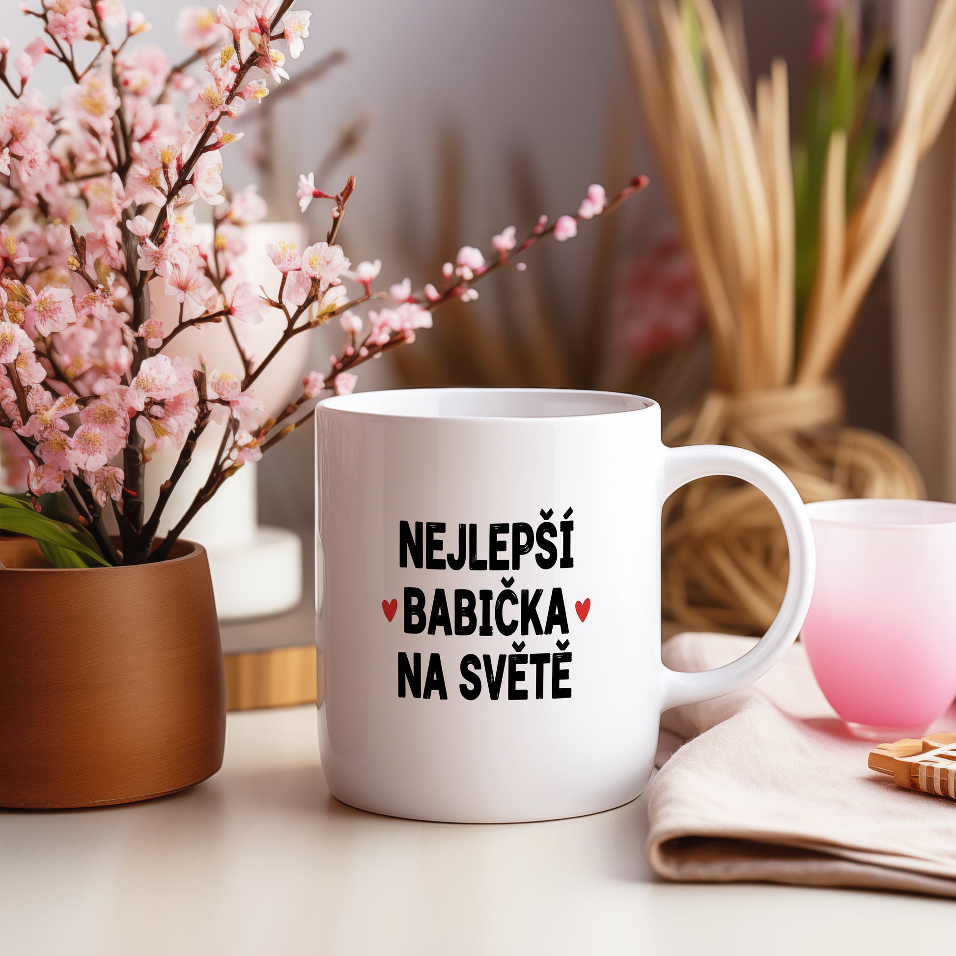 Bílý hrnek s nápisem NEJLEPŠÍ BABIČKA NA SVĚTĚ a červenými srdíčky.