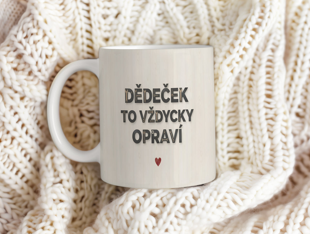 Bílý hrnek s nápisem 'DĚDEČEK TO VŽDYCKY OPRAVÍ' a červeným srdcem na dřevěném pozadí.