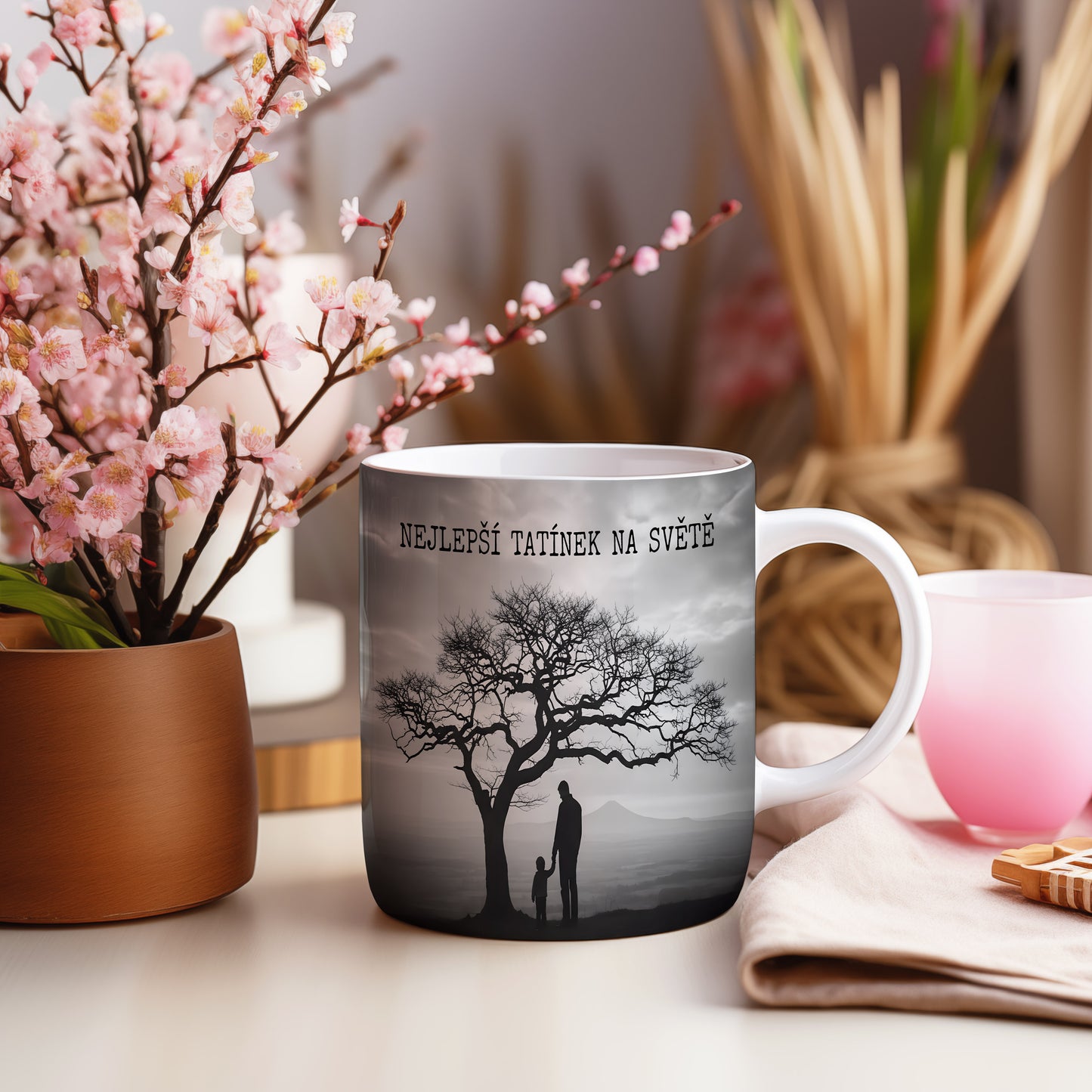 Hrnek s černobílou siluetou otce a dítěte pod stromem.
