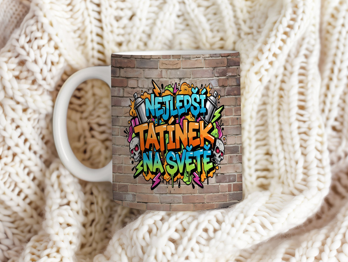 Hrnek s grafitti nápisem NEJLEPŠÍ TATÍNEK NA SVĚTĚ na cihlovém pozadí.