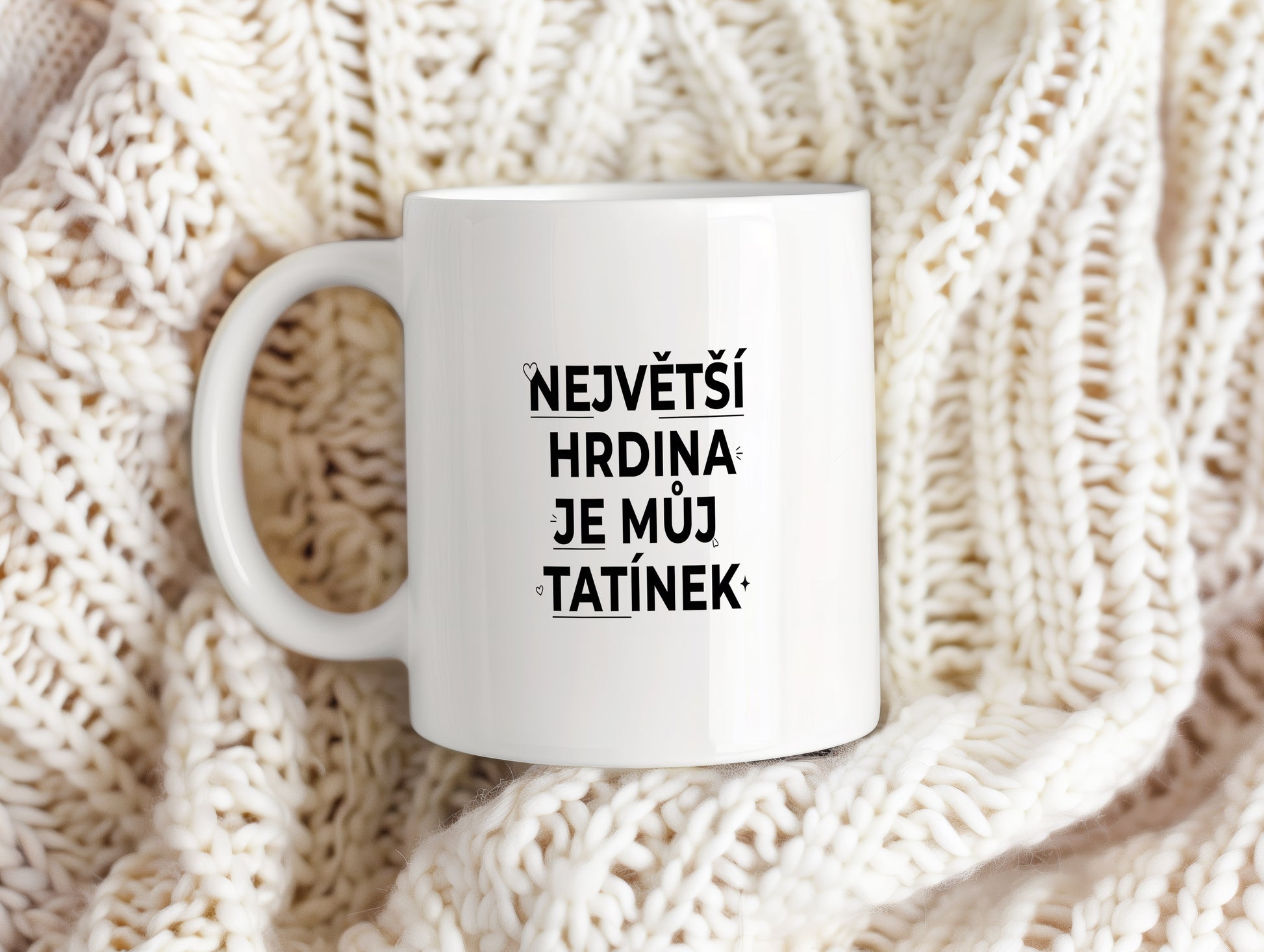 Bílý hrnek s černým nápisem 'NEJVĚTŠÍ HRDINA JE MŮJ TATÍNEK' a malými srdíčky.
