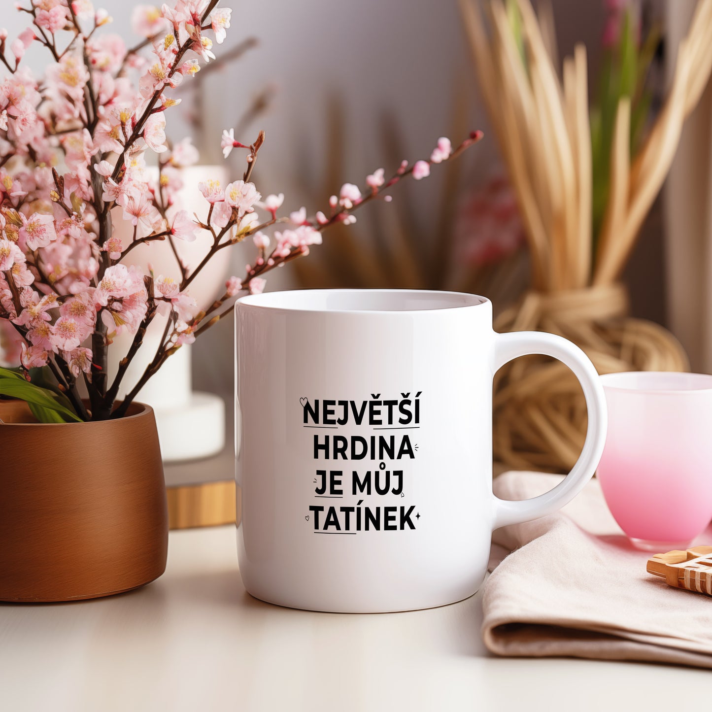 Bílý hrnek s černým nápisem 'NEJVĚTŠÍ HRDINA JE MŮJ TATÍNEK' a malými srdíčky.