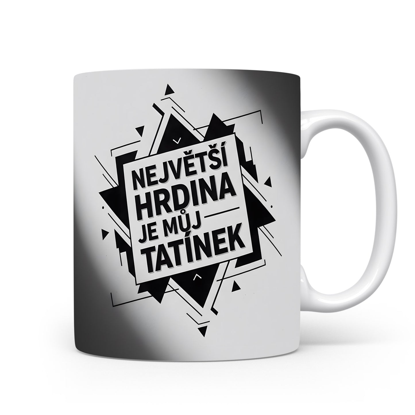 Bílý hrnek s černým nápisem 'NEJVĚTŠÍ HRDINA JE MŮJ TATÍNEK' a geometrickým vzorem.