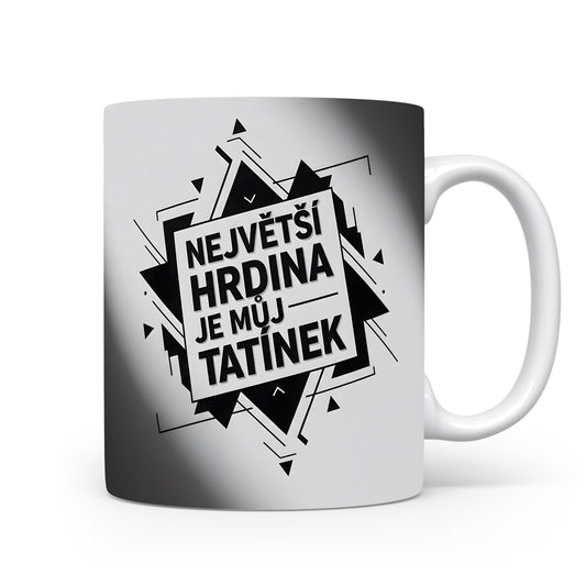 Bílý hrnek s černým nápisem 'NEJVĚTŠÍ HRDINA JE MŮJ TATÍNEK' a geometrickým vzorem.
