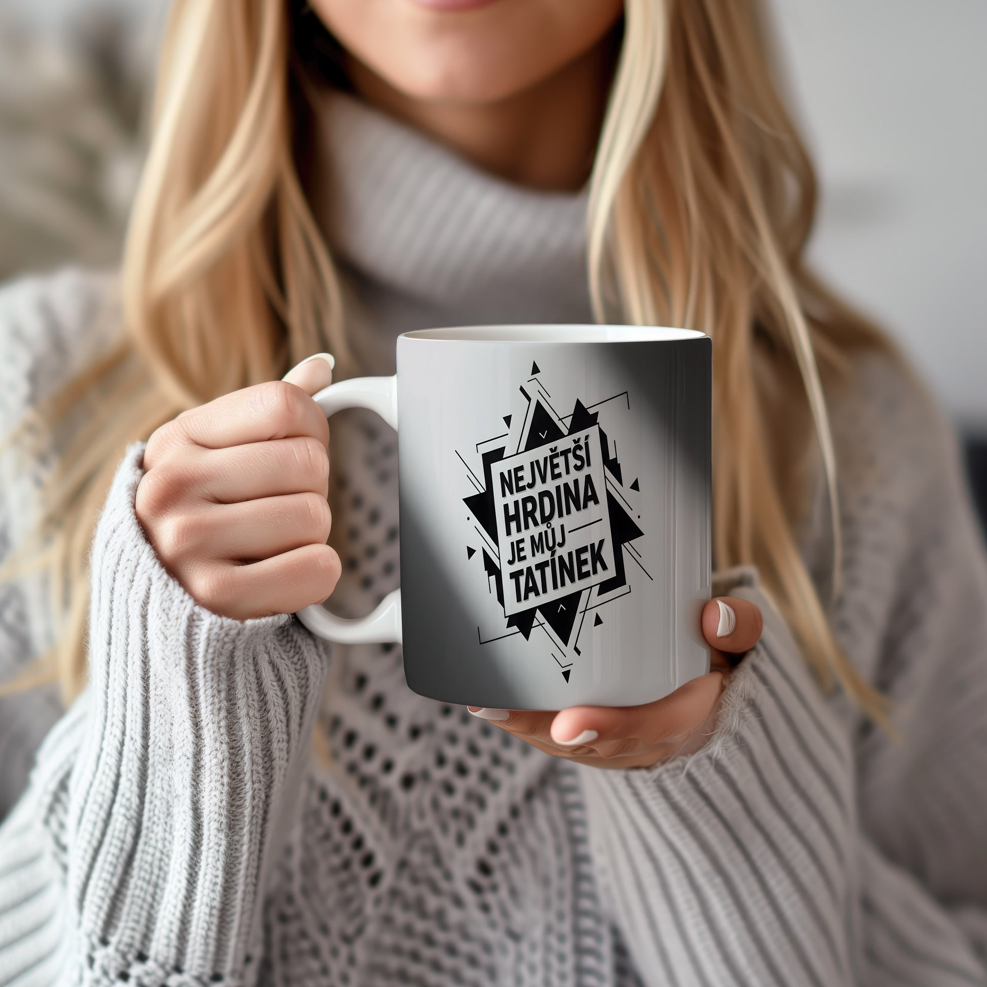 Bílý hrnek s černým nápisem 'NEJVĚTŠÍ HRDINA JE MŮJ TATÍNEK' a geometrickým vzorem.