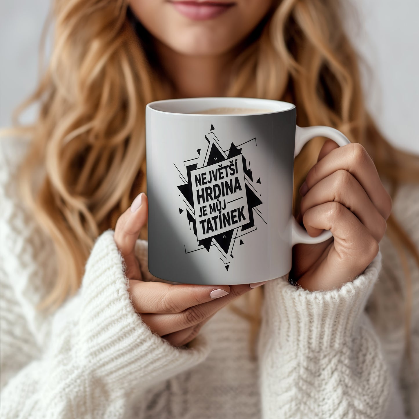 Bílý hrnek s černým nápisem 'NEJVĚTŠÍ HRDINA JE MŮJ TATÍNEK' a geometrickým vzorem.