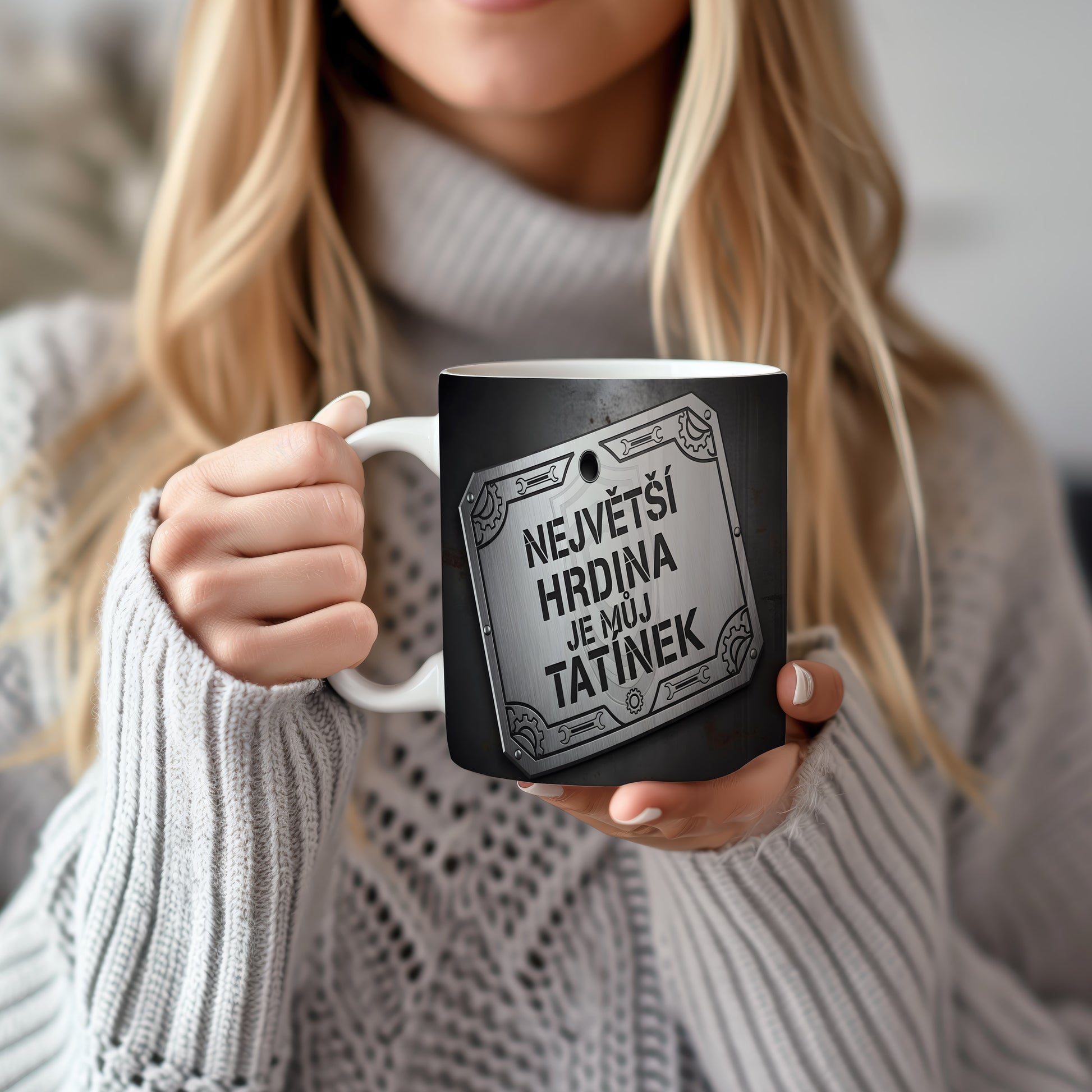 Černý hrnek s kovovým štítem a nápisem 'NEJVĚTŠÍ HRDINA JE MŮJ TATÍNEK'.
