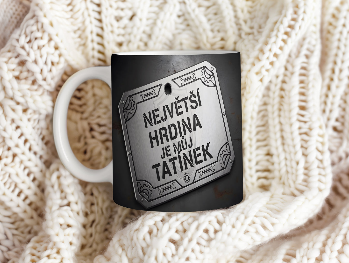 Černý hrnek s kovovým štítem a nápisem 'NEJVĚTŠÍ HRDINA JE MŮJ TATÍNEK'.