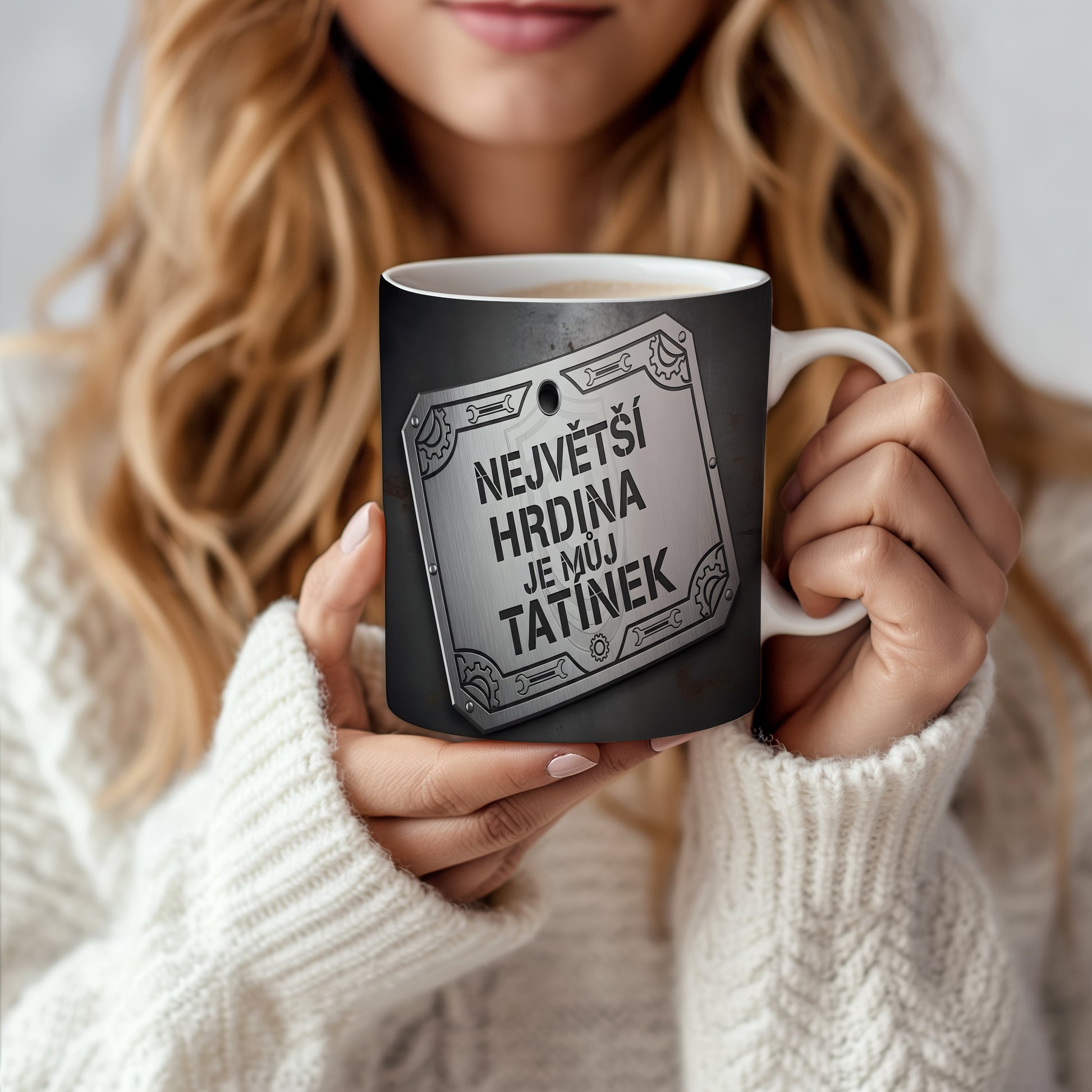 Černý hrnek s kovovým štítem a nápisem 'NEJVĚTŠÍ HRDINA JE MŮJ TATÍNEK'.