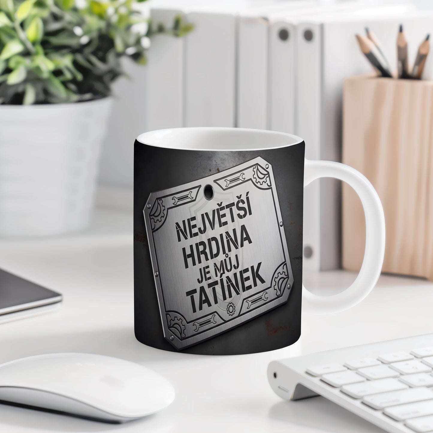 Černý hrnek s kovovým štítem a nápisem 'NEJVĚTŠÍ HRDINA JE MŮJ TATÍNEK'.