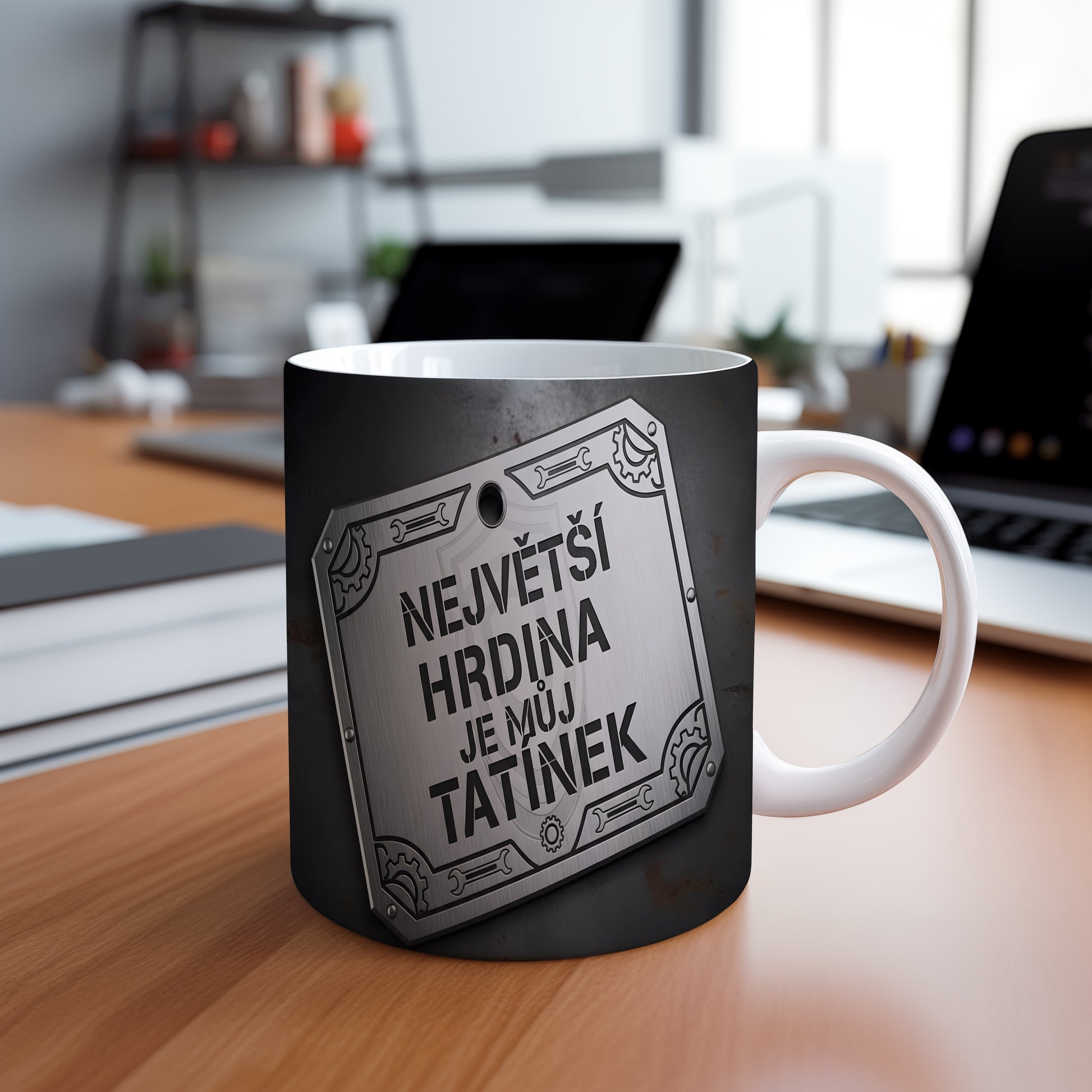 Černý hrnek s kovovým štítem a nápisem 'NEJVĚTŠÍ HRDINA JE MŮJ TATÍNEK'.