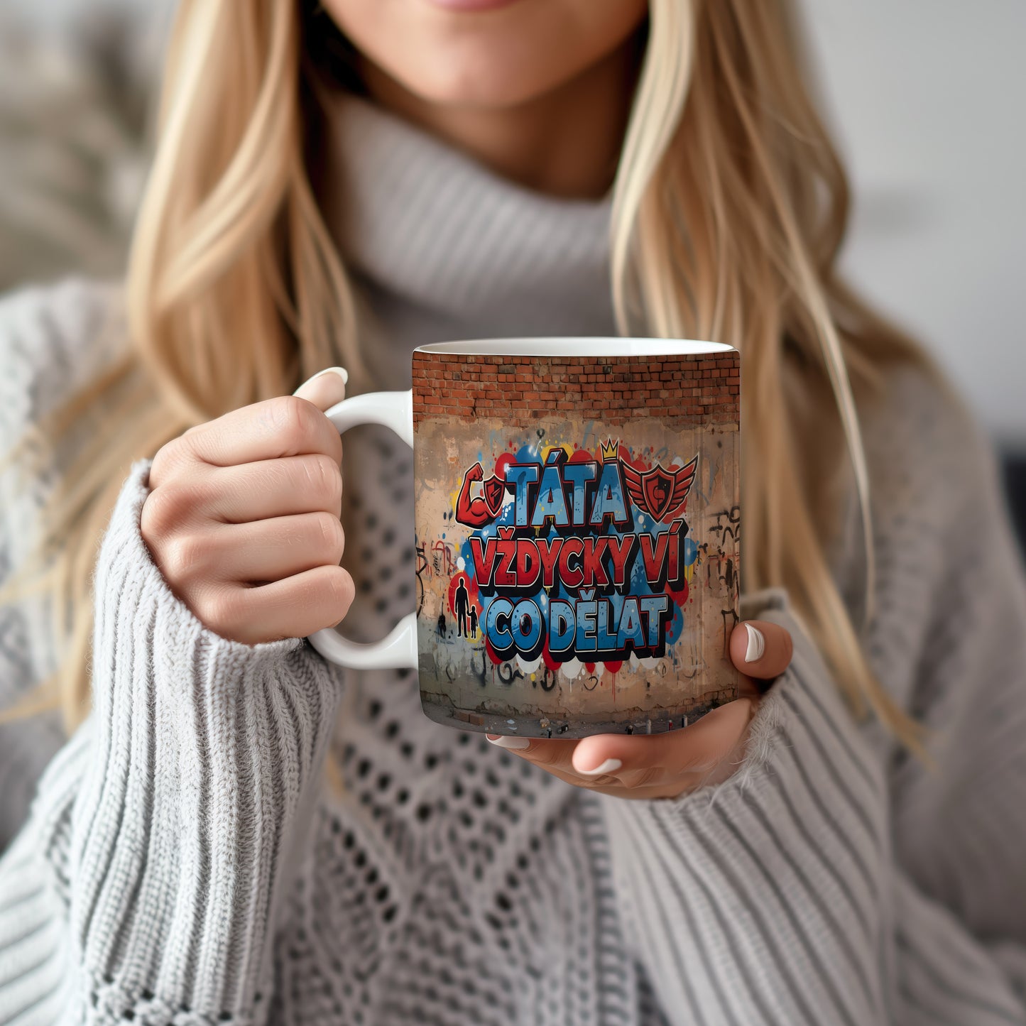 Hrnek s nápisem TÁTA VŽDYCKY VÍ CO DĚLAT na cihlové zdi s grafitti.
