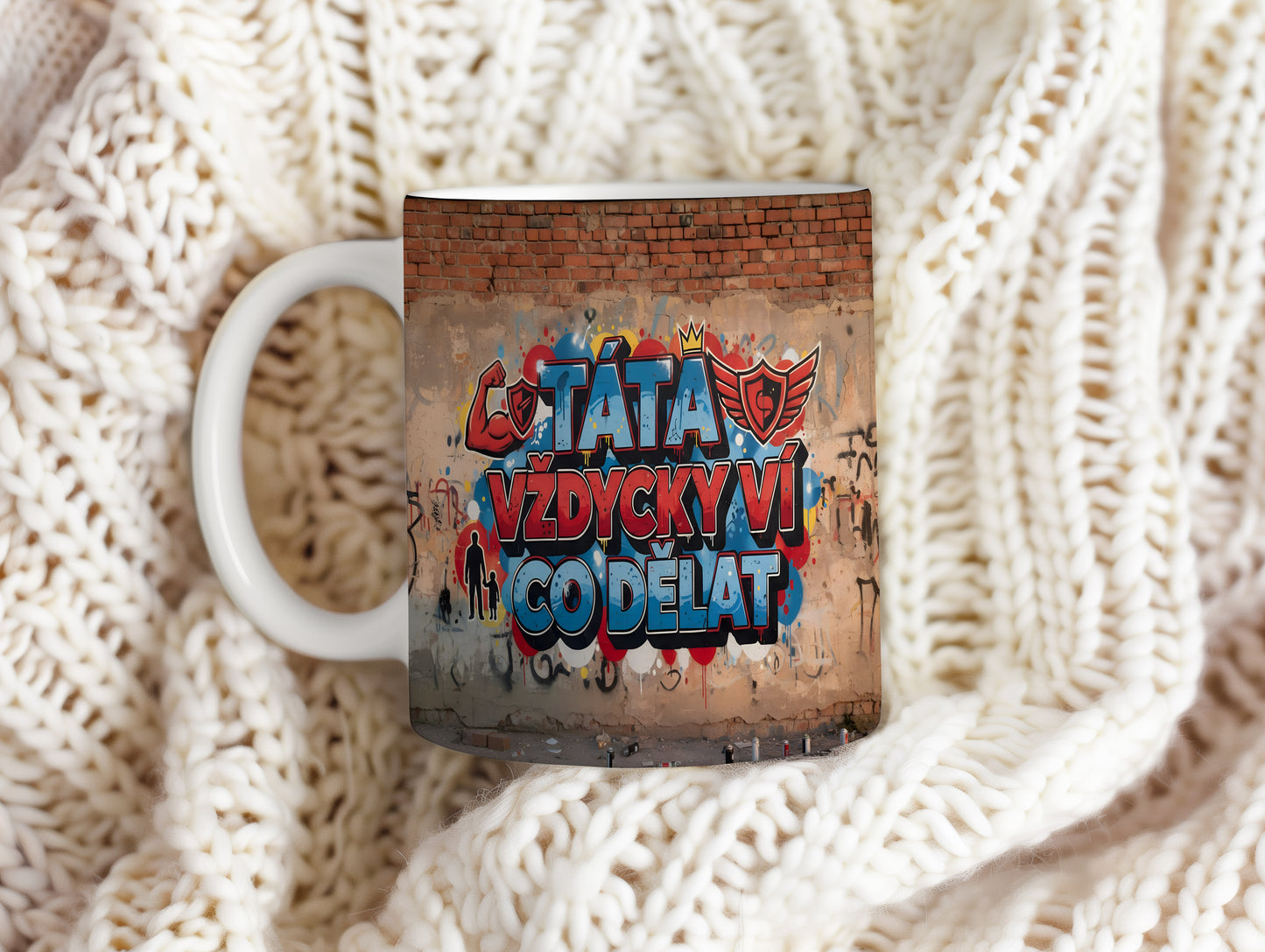 Hrnek s nápisem TÁTA VŽDYCKY VÍ CO DĚLAT na cihlové zdi s grafitti.