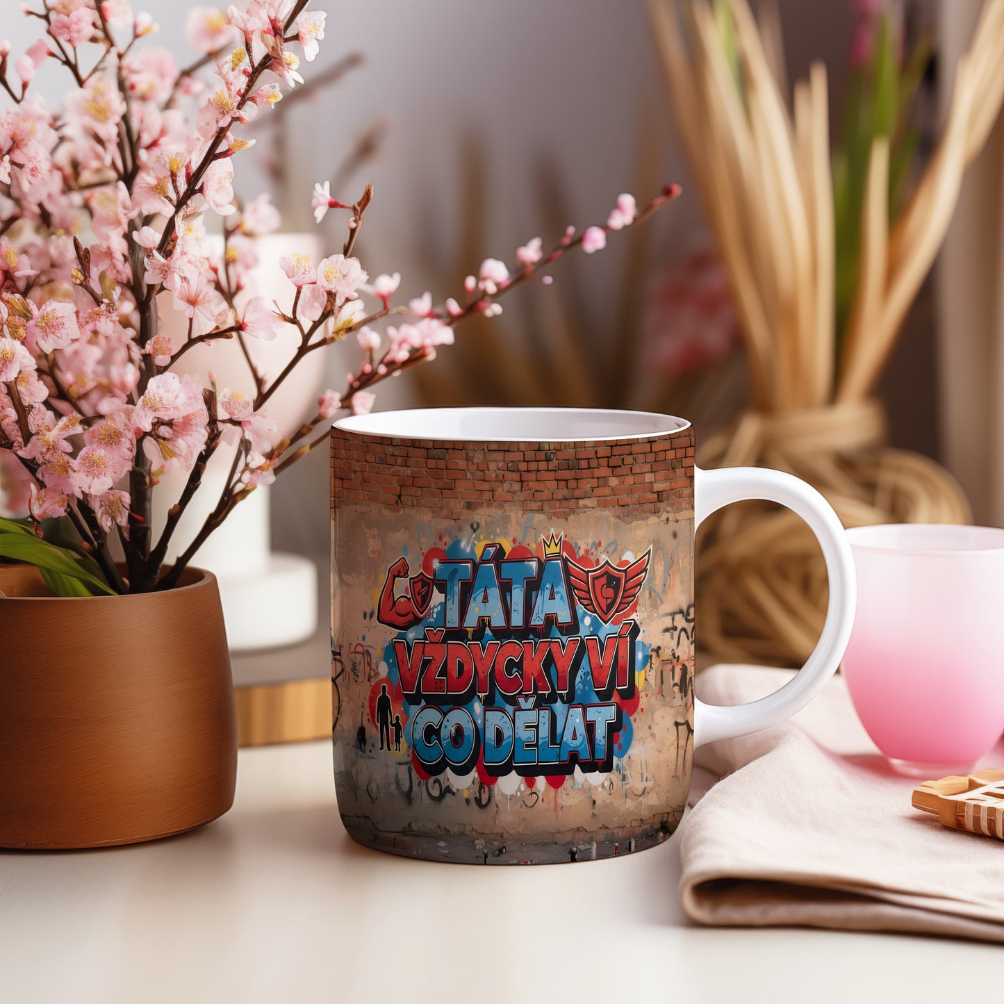 Hrnek s nápisem TÁTA VŽDYCKY VÍ CO DĚLAT na cihlové zdi s grafitti.