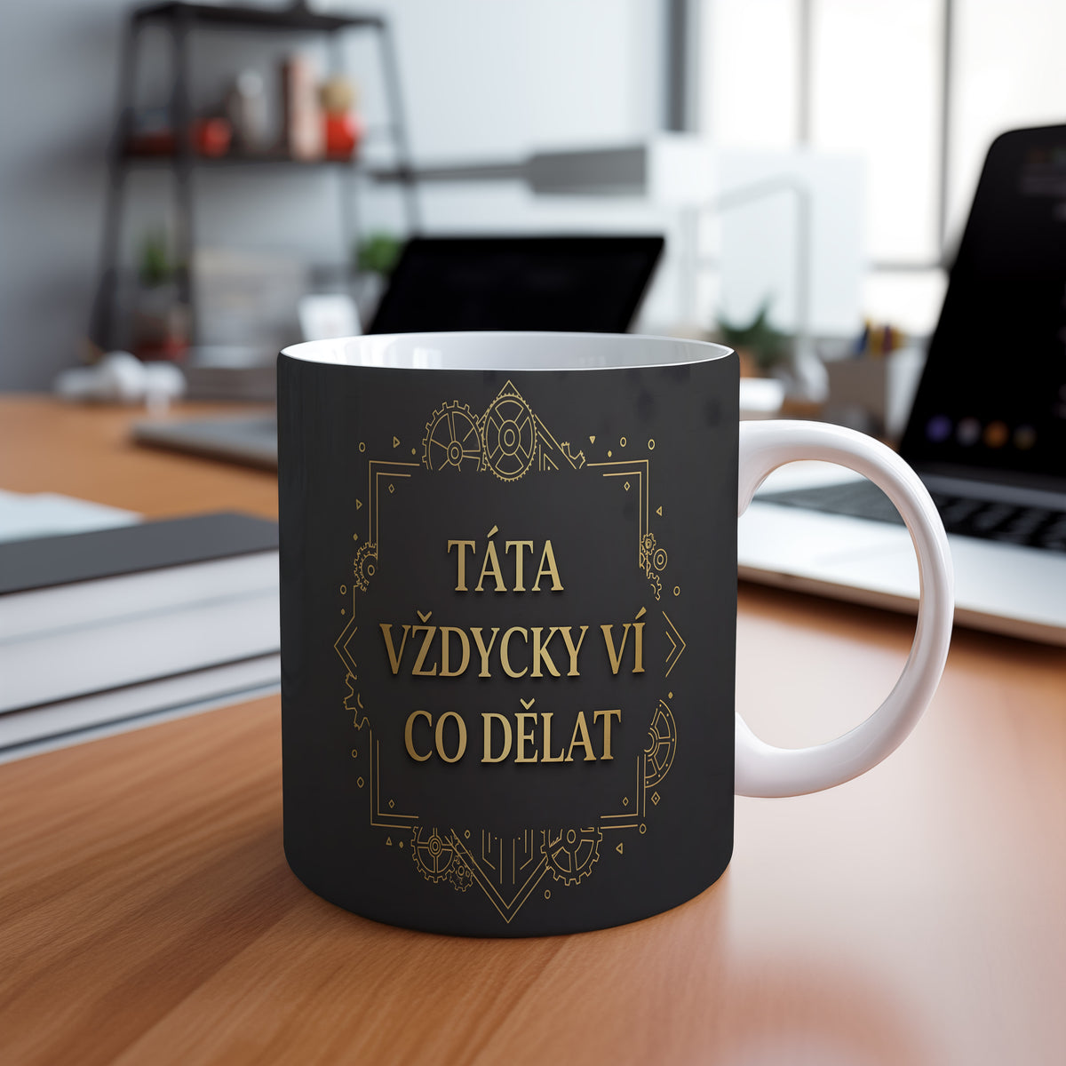 Černý hrnek se zlatým textem a technickým vzorem.