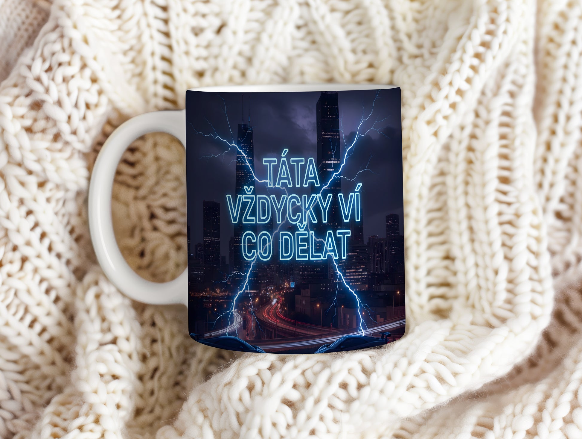 Hrnek s nápisem 'TÁTA VŽDYCKY VÍ CO DĚLAT' a blesky na pozadí města.