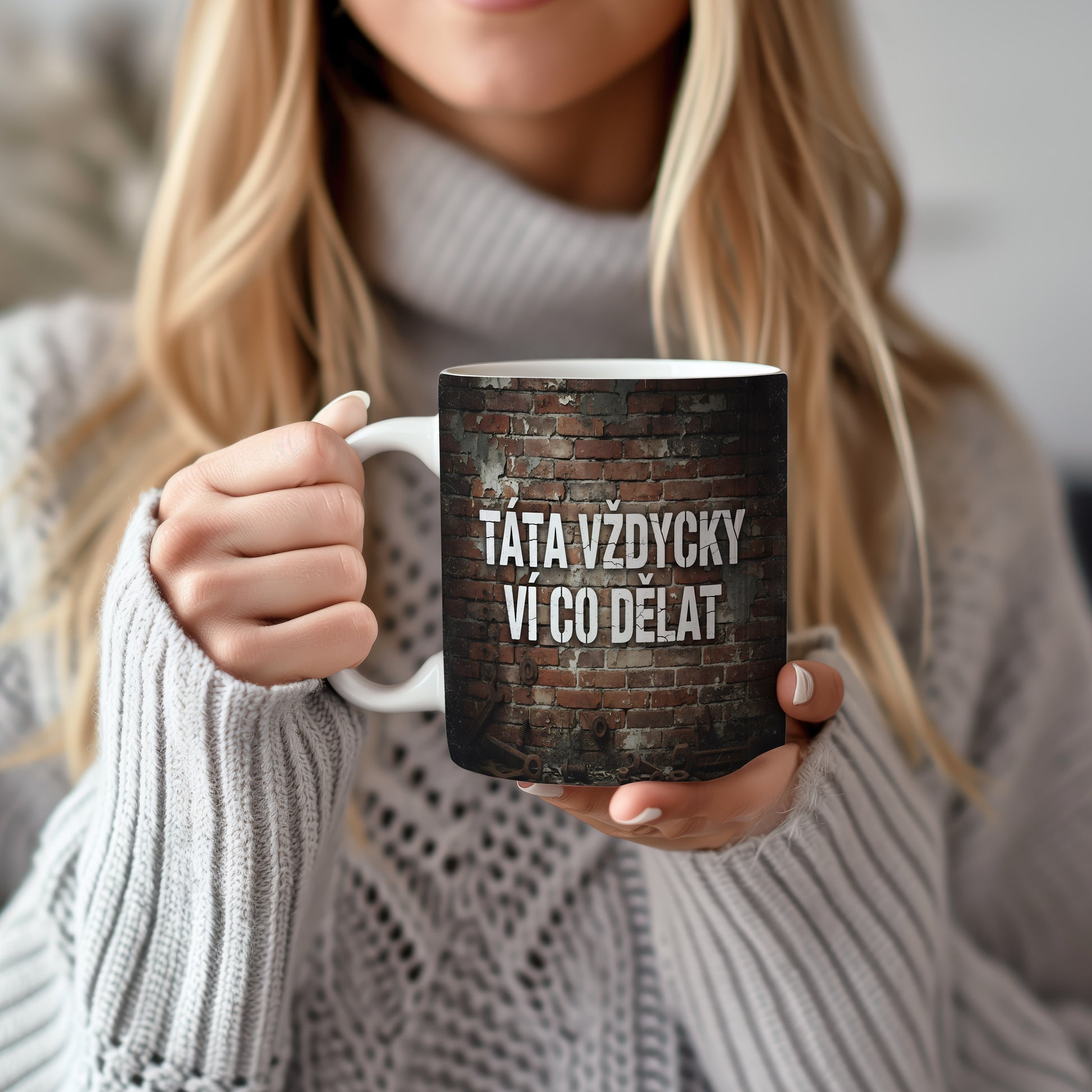 Hrnek s nápisem 'TÁTA VŽDYCKY VÍ CO DĚLAT' na cihlovém pozadí.
