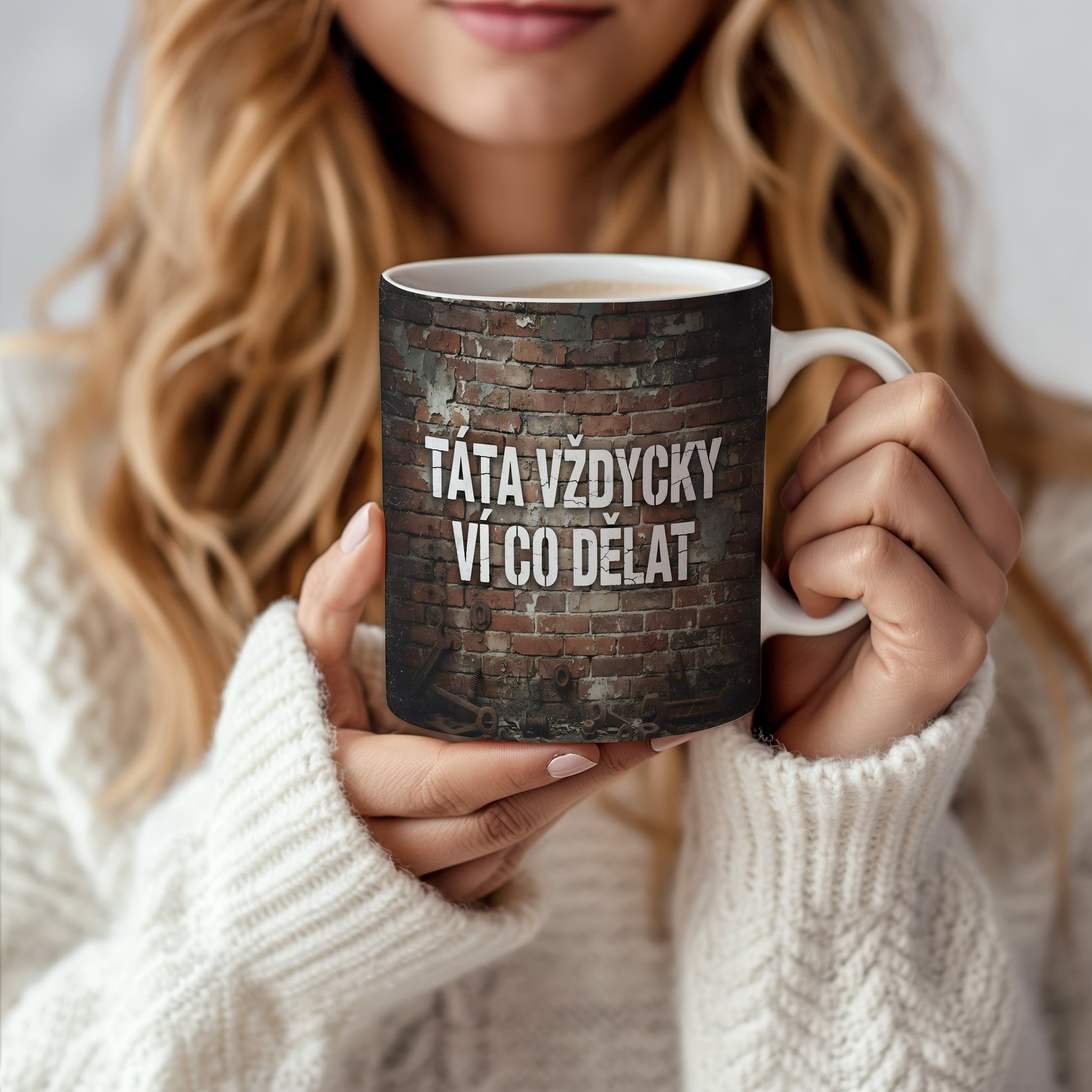 Hrnek s nápisem 'TÁTA VŽDYCKY VÍ CO DĚLAT' na cihlovém pozadí.