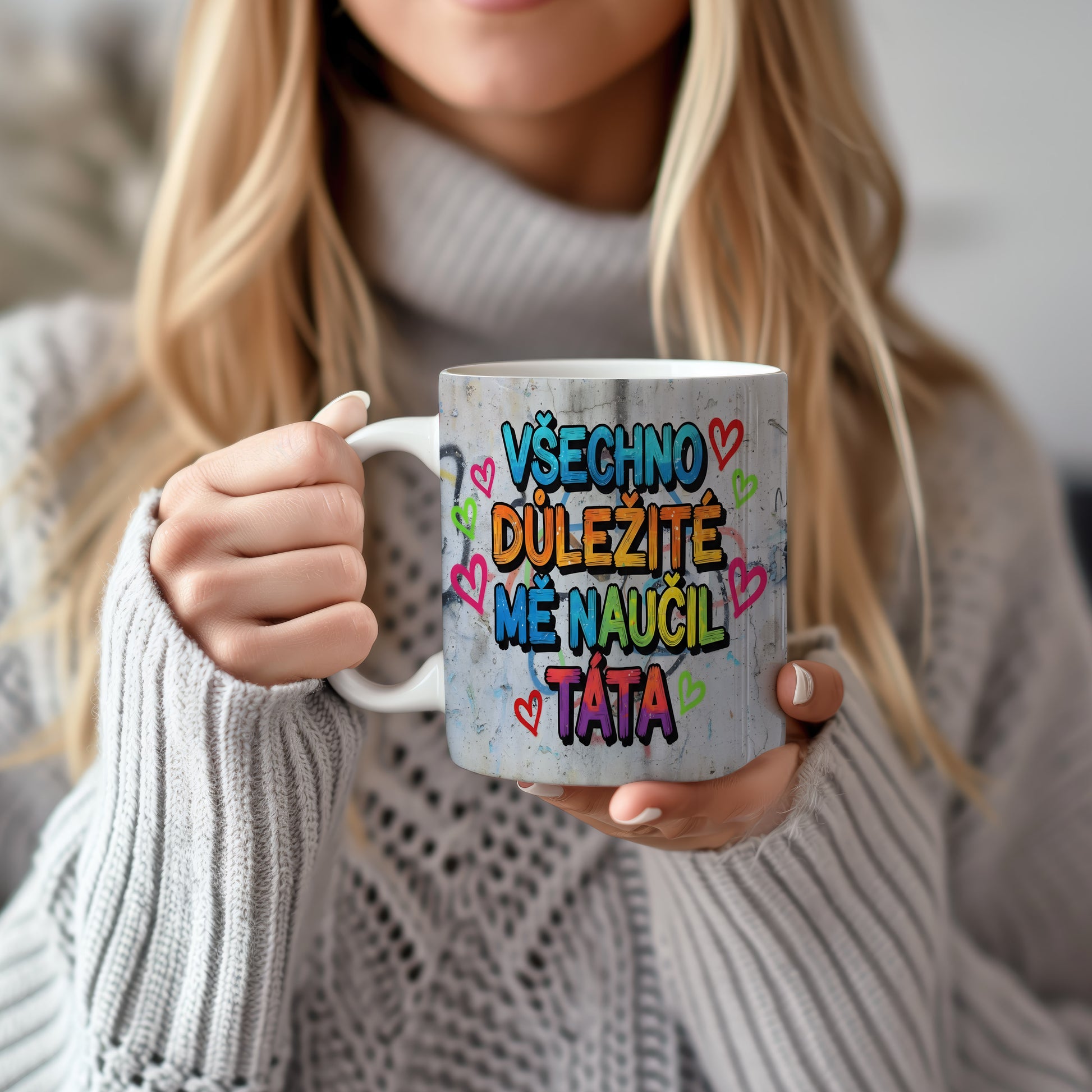 Hrnek s barevným nápisem a srdíčky na betonovém pozadí.