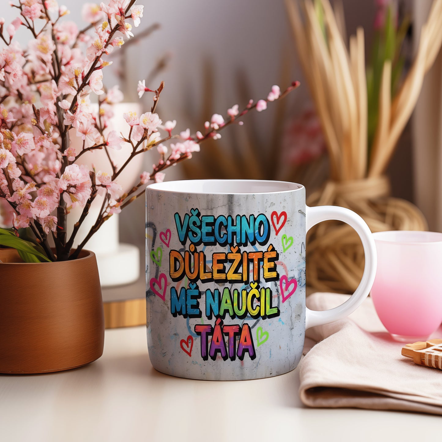 Hrnek s barevným nápisem a srdíčky na betonovém pozadí.