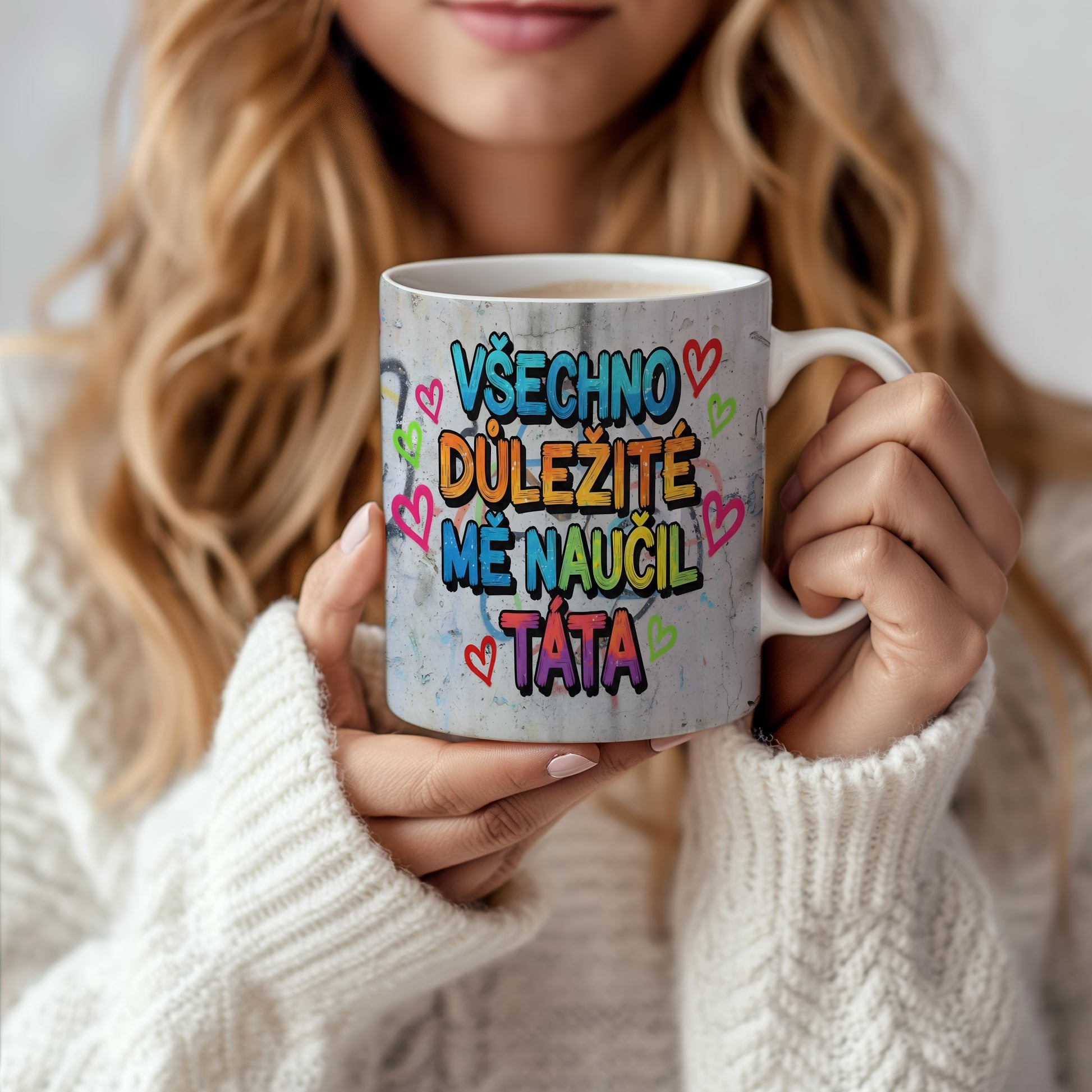 Hrnek s barevným nápisem a srdíčky na betonovém pozadí.