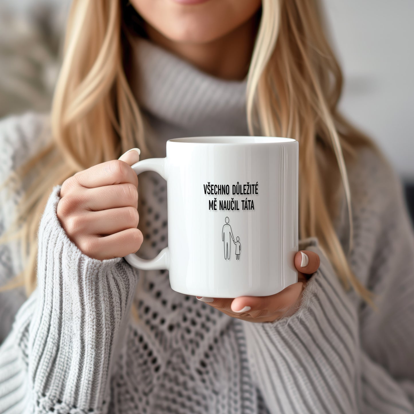 Bílý hrnek s černým nápisem a minimalistickými postavami.