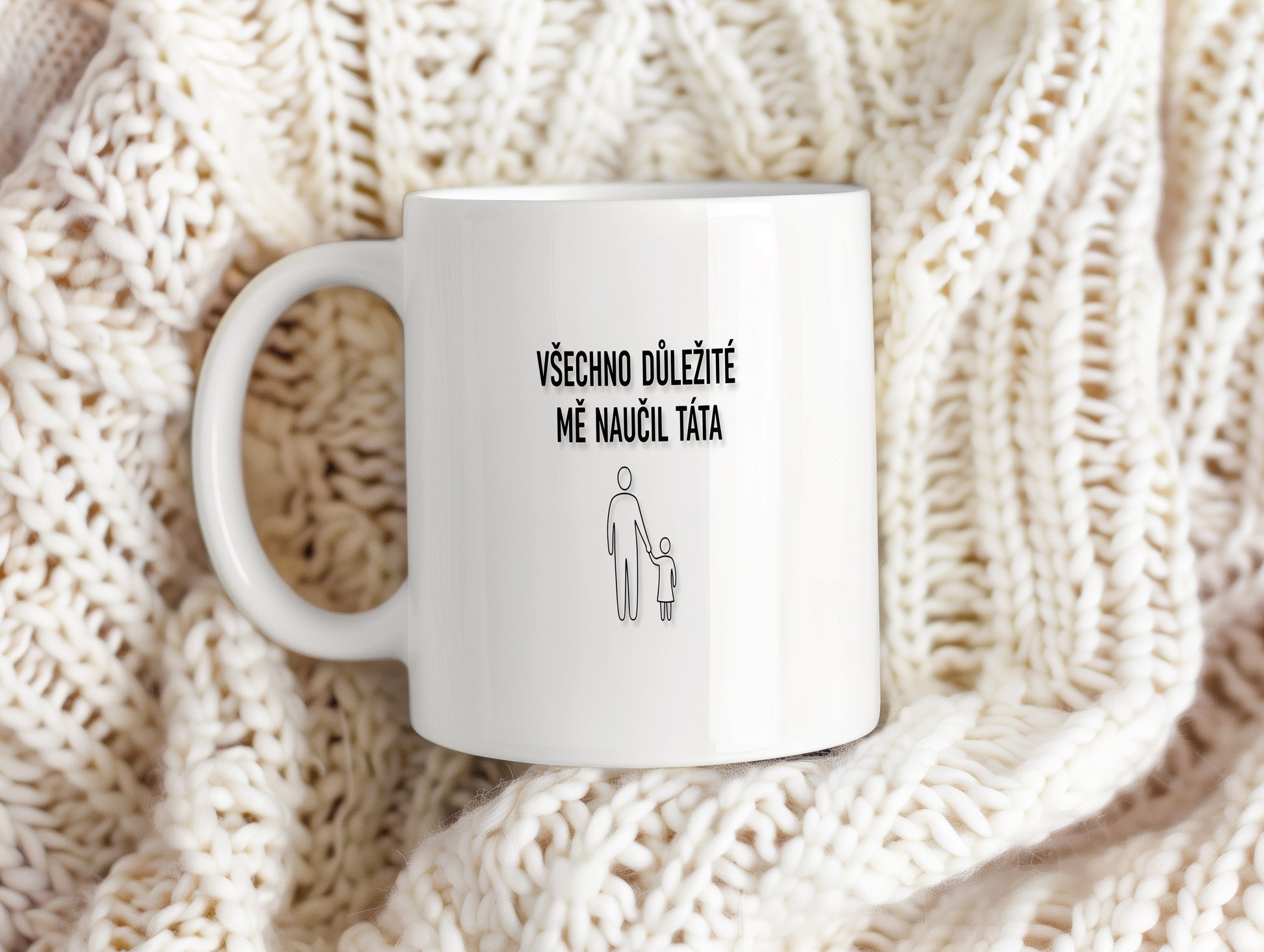 Bílý hrnek s černým nápisem a minimalistickými postavami.