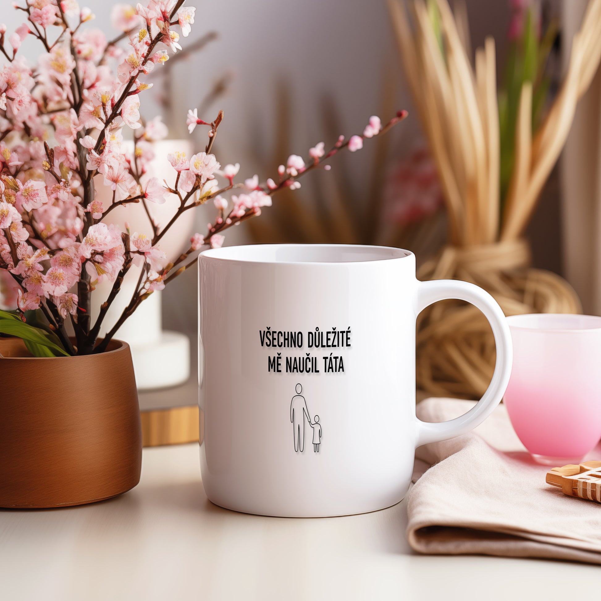Bílý hrnek s černým nápisem a minimalistickými postavami.