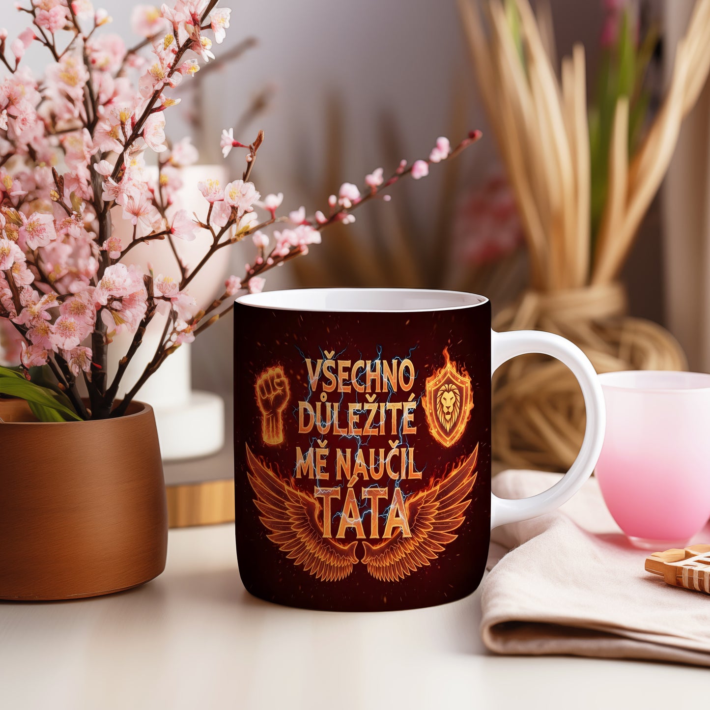 Černý hrnek s oranžovými motivy křídel, pěsti a lva.