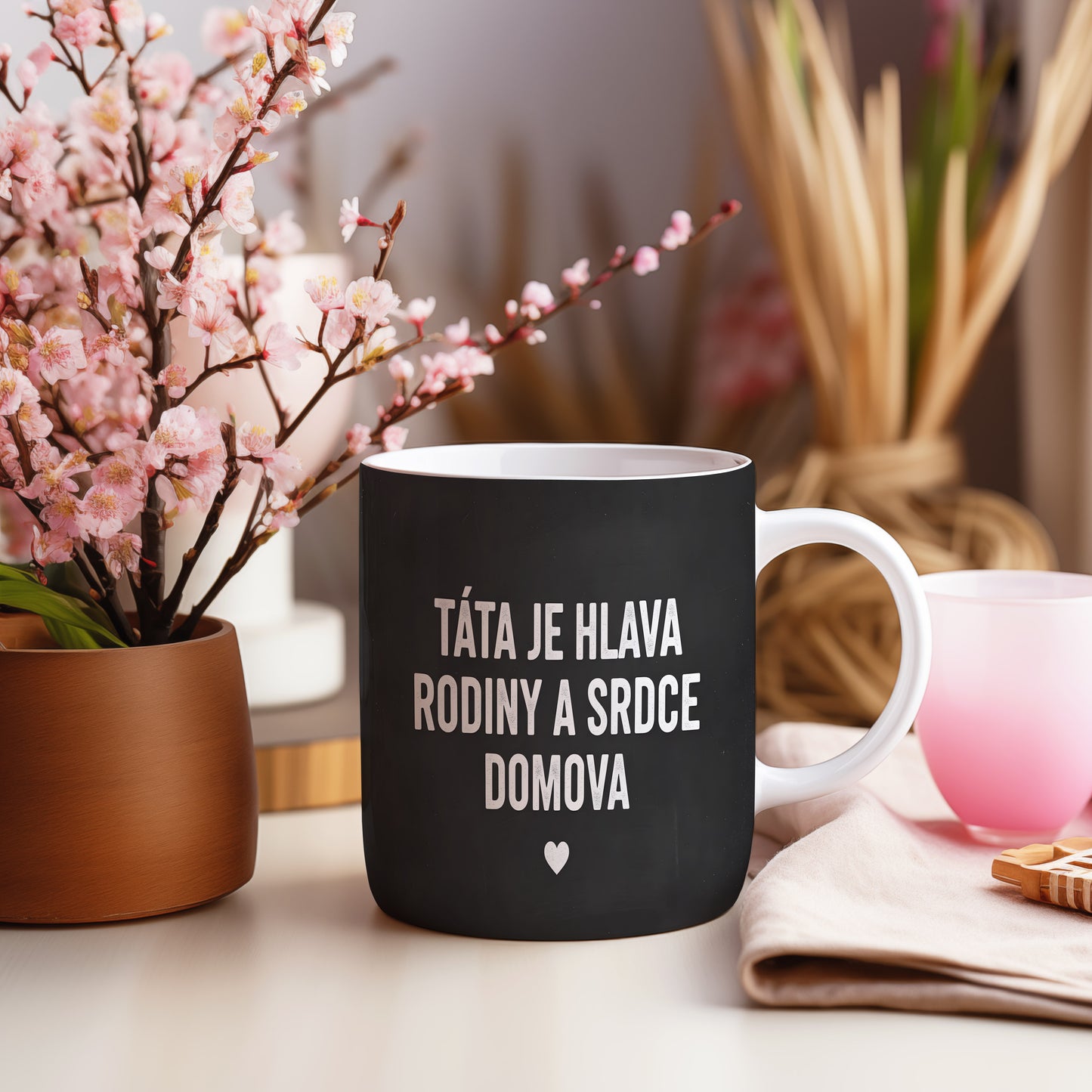 Černý hrnek s bílým nápisem TÁTA JE HLAVA RODINY A SRDCE DOMOVA a malým srdcem.
