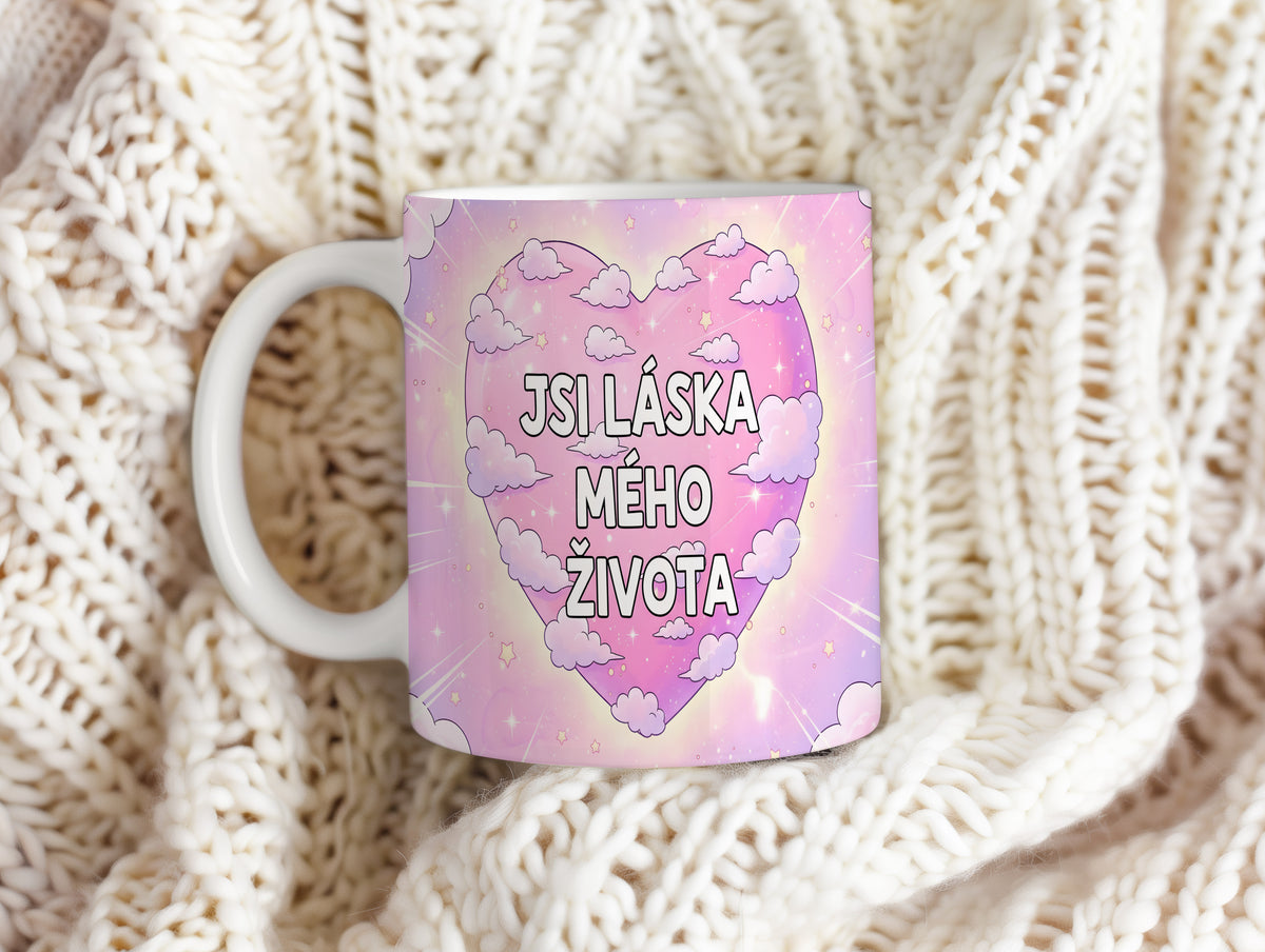 Růžový hrnek s nápisem JSI LÁSKA MÉHO ŽIVOTA obklopený mraky a hvězdami.